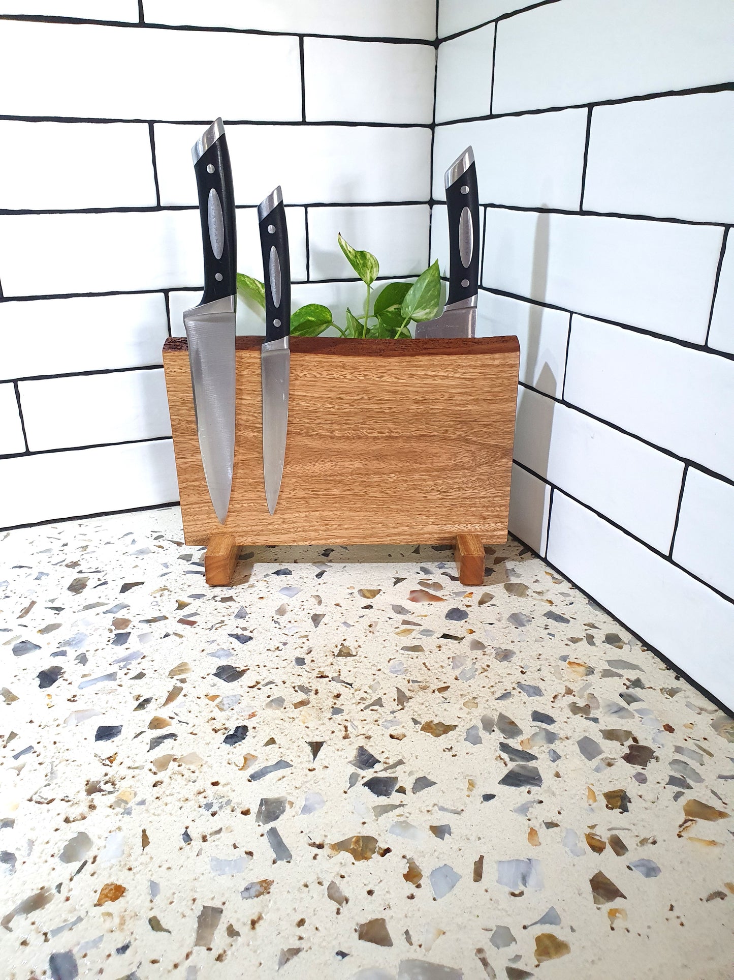 Wooden knife block with knives on a terrazzo floor against a tiled wall.