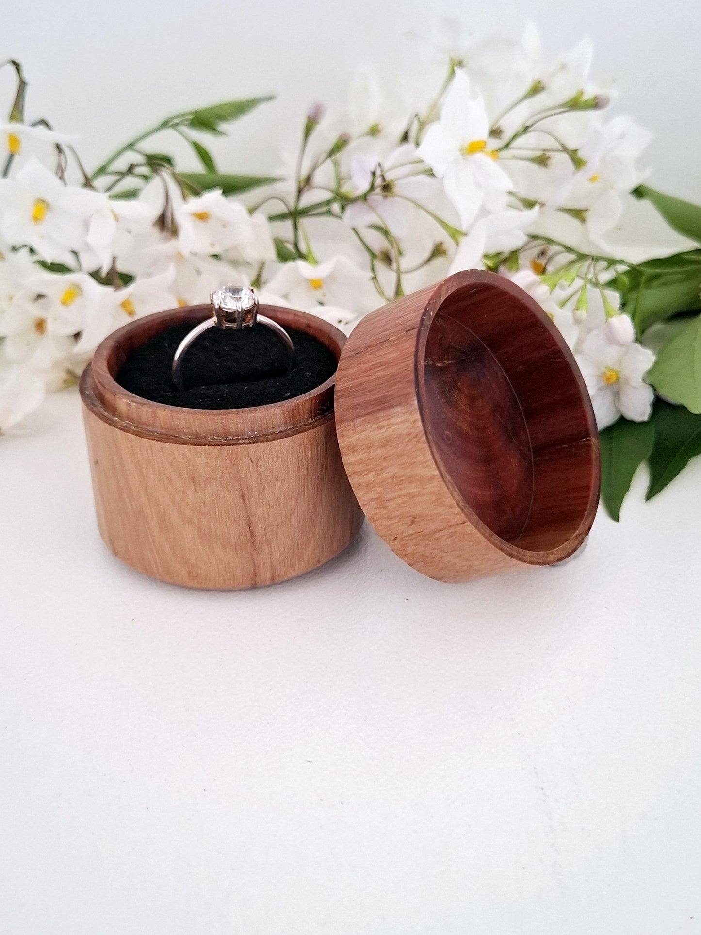 Wooden ring box with a ring inside, surrounded by white flowers on a light background