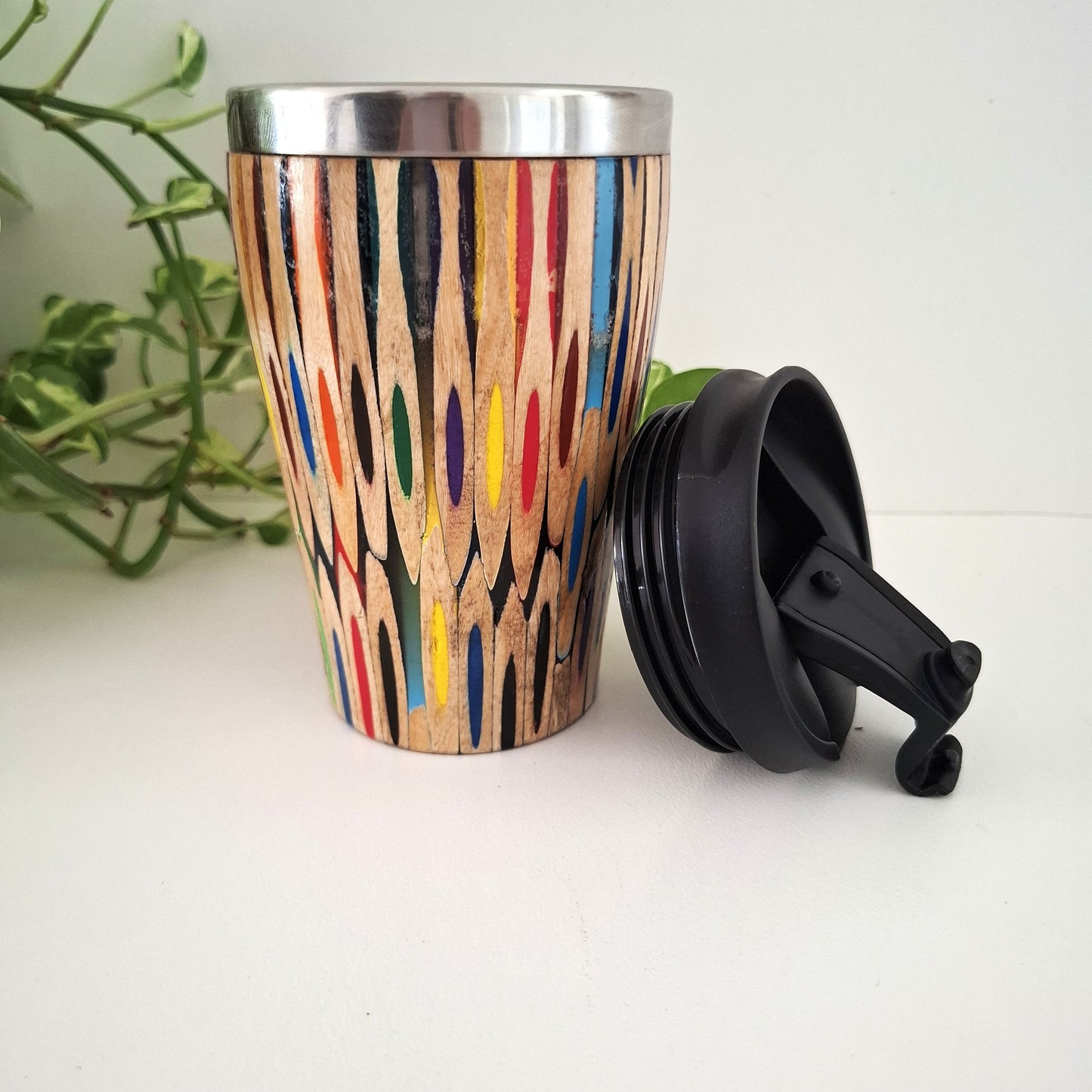Wooden tumbler with colorful patterns and a black lid on a white surface.