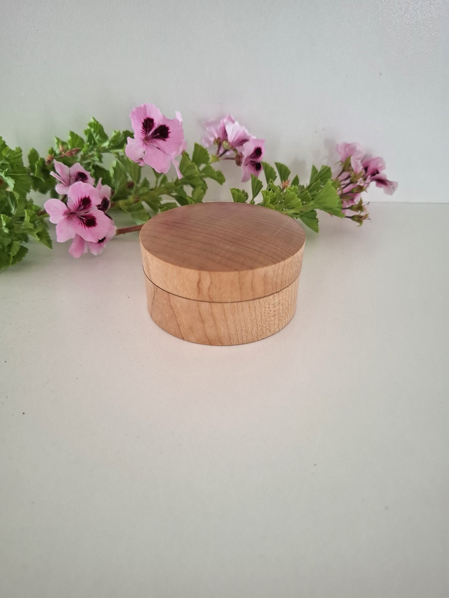 Wooden box with a lid on a white surface with pink flowers in the background