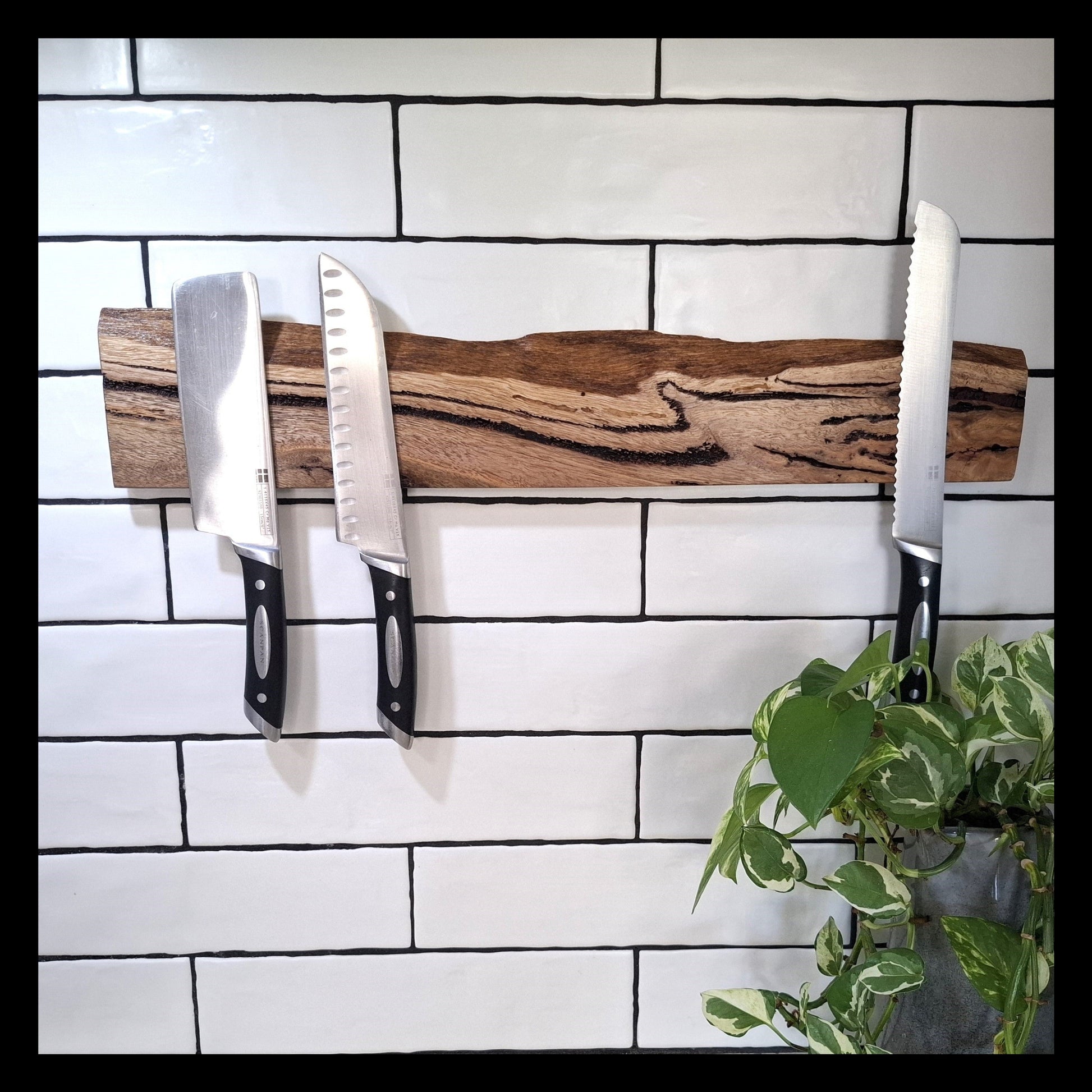 Wooden knife holder with three knives against a white tiled wall.