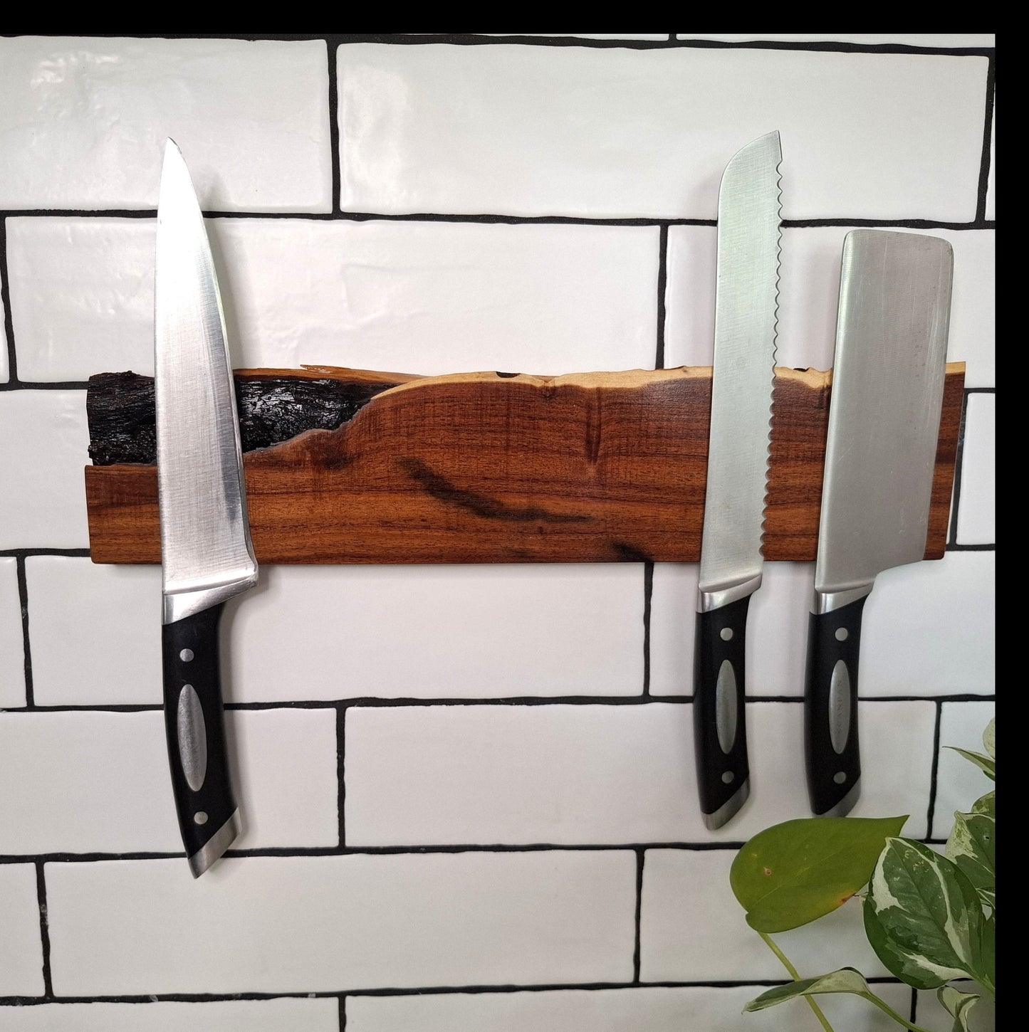 Three knives on a magnetic wooden strip against a tiled wall.