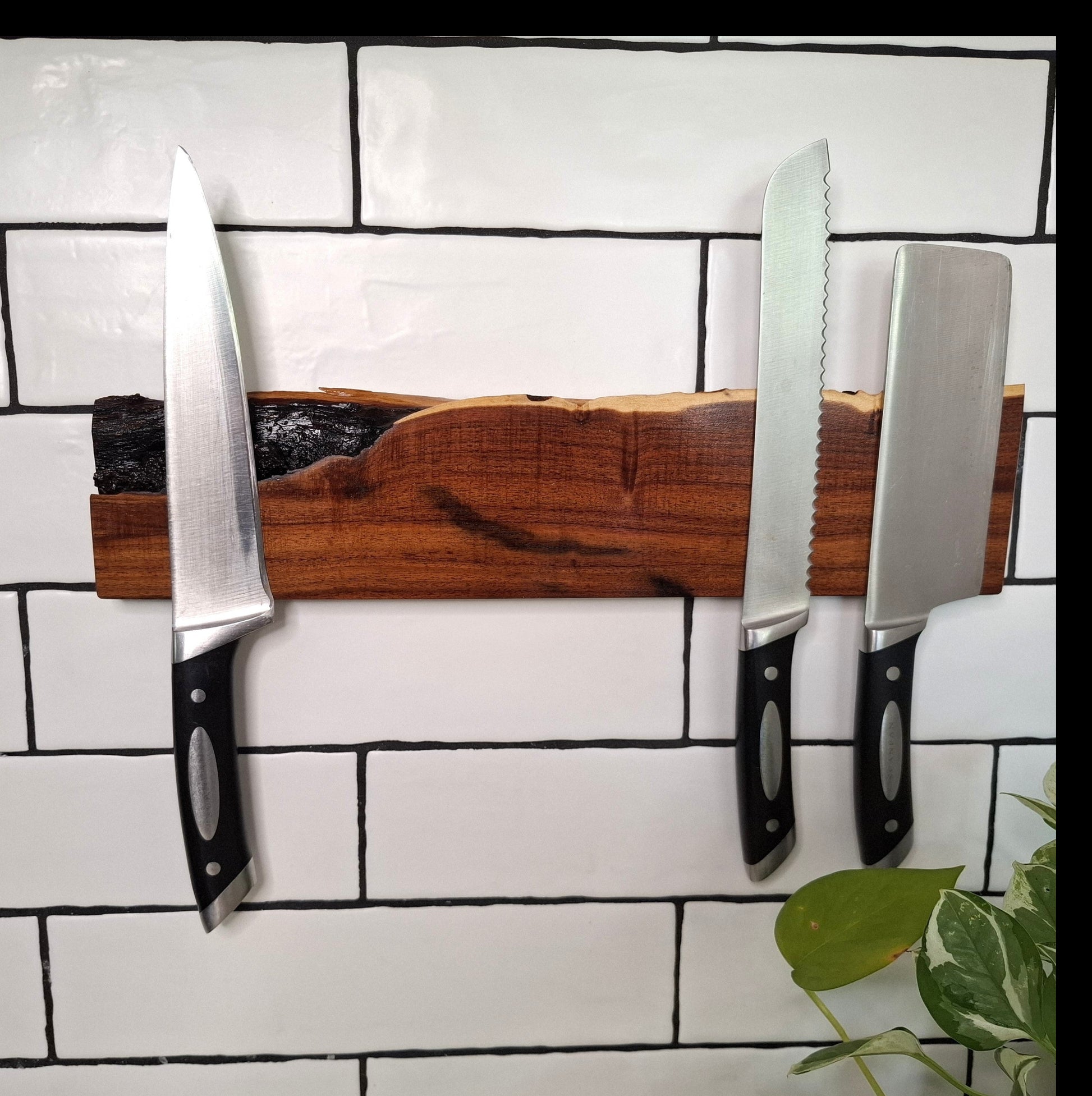 Three knives on a magnetic wooden strip against a tiled wall.
