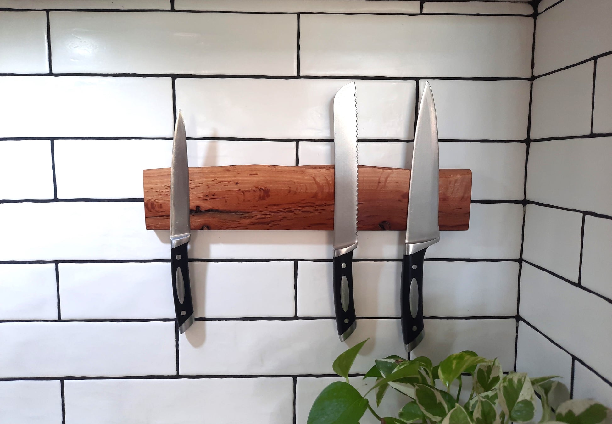 Set of knives on a wooden magnetic strip against a tiled wall.