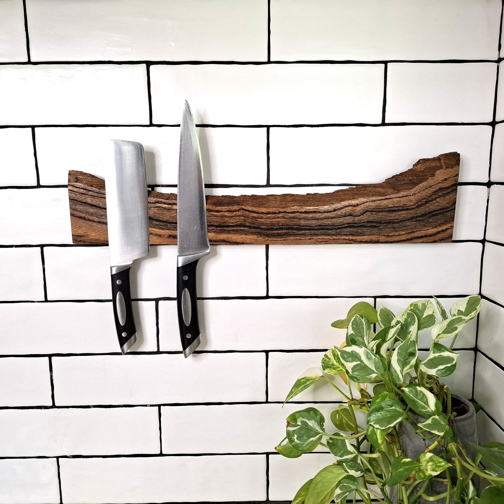 Wooden knife holder with knives on a tiled wall, next to a potted plant.