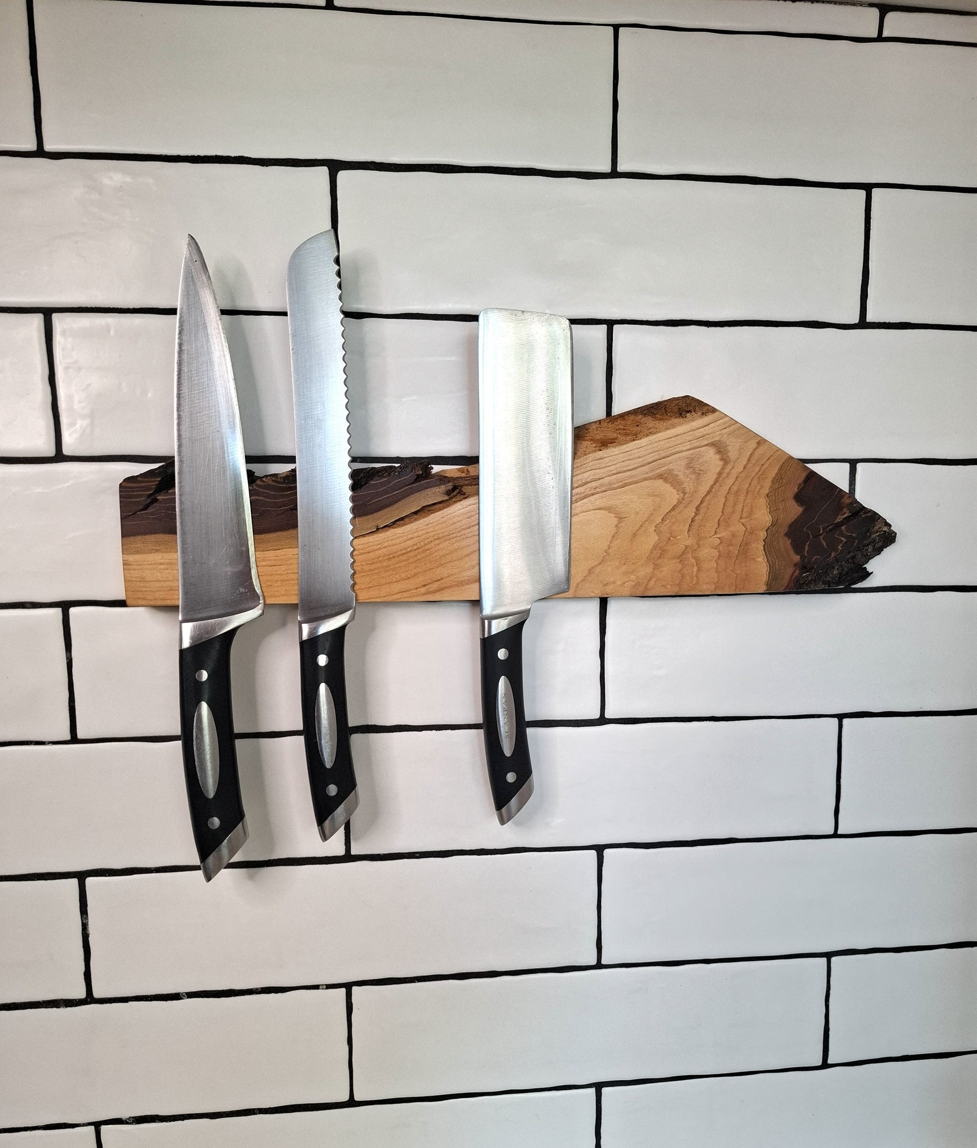 Set of three knives on a wooden block against a tiled wall background
