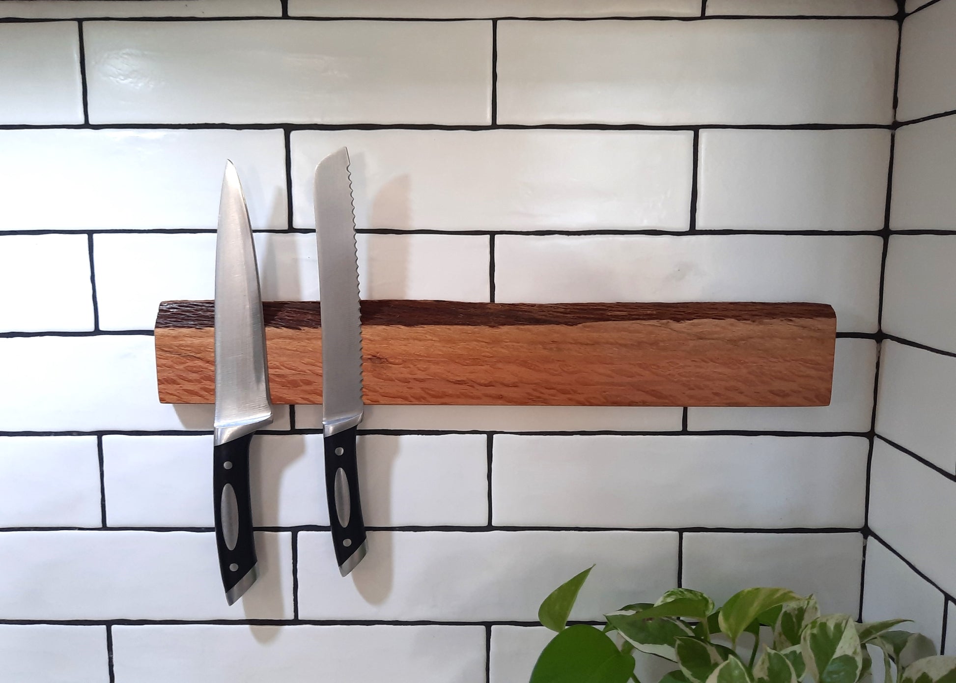 Two knives on a wooden magnetic strip against a tiled wall.