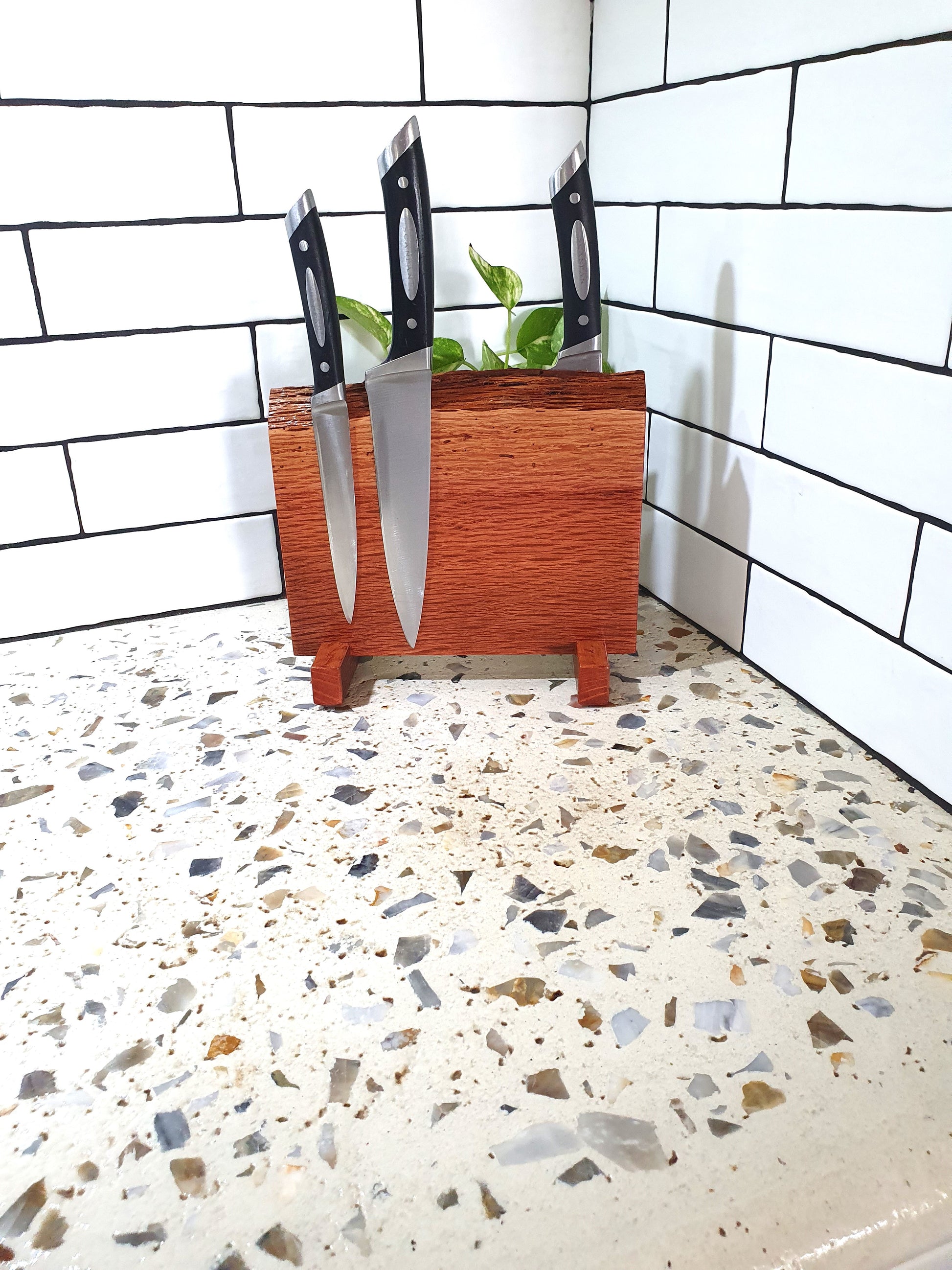 Wooden knife block with knives on a speckled countertop against a tiled wall.