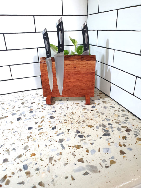 Wooden knife block with knives on a speckled countertop against a tiled wall.