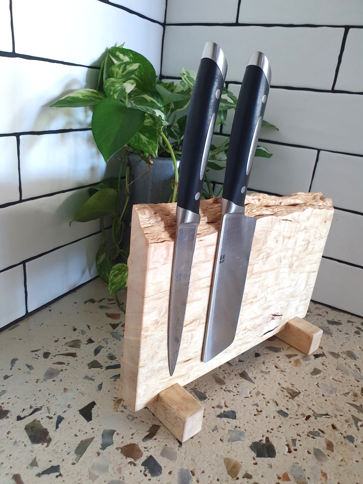 Two knives in a wooden block on a speckled countertop with a tiled wall background.