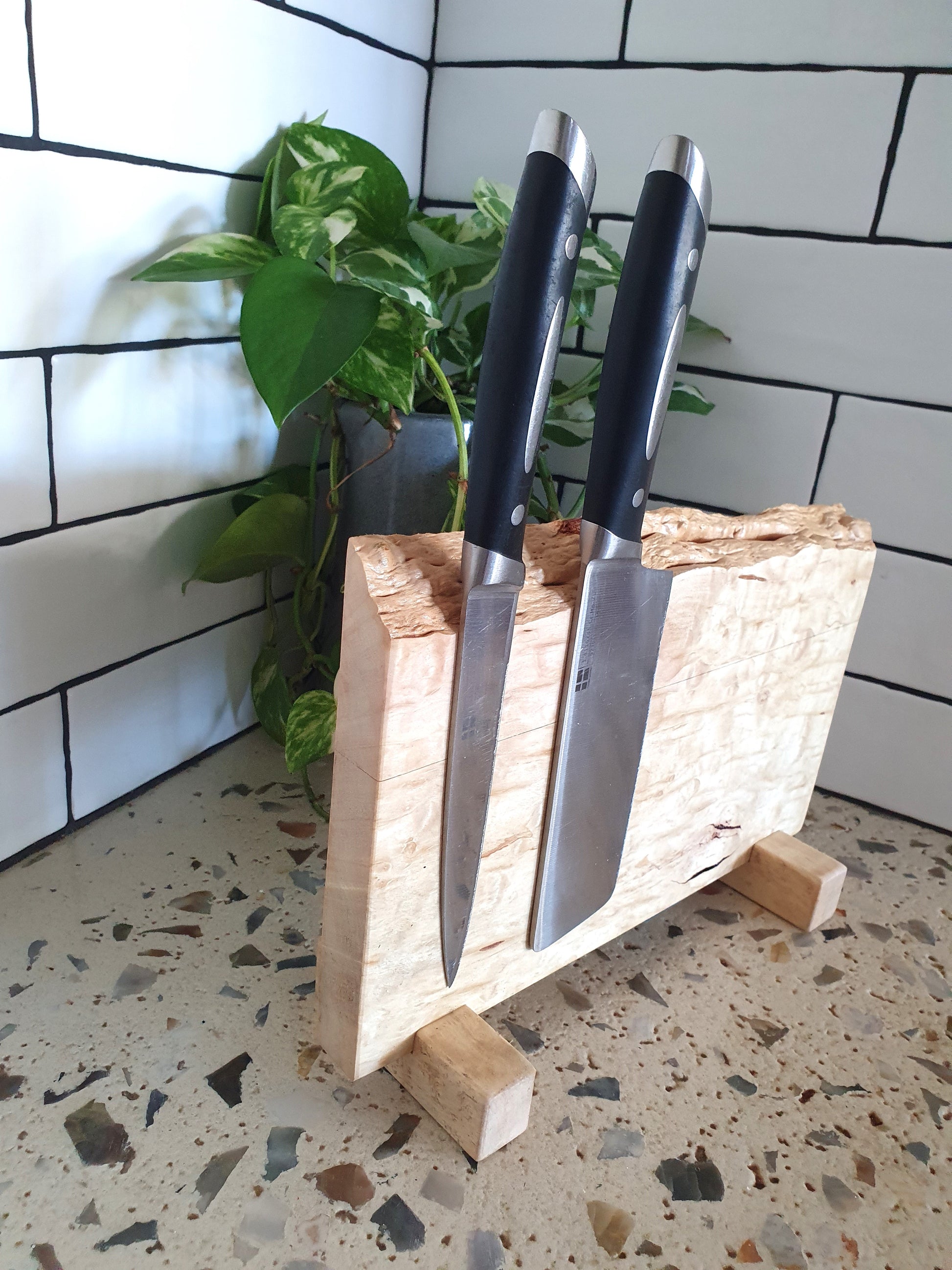 Two knives in a wooden block on a speckled countertop with a tiled wall background.