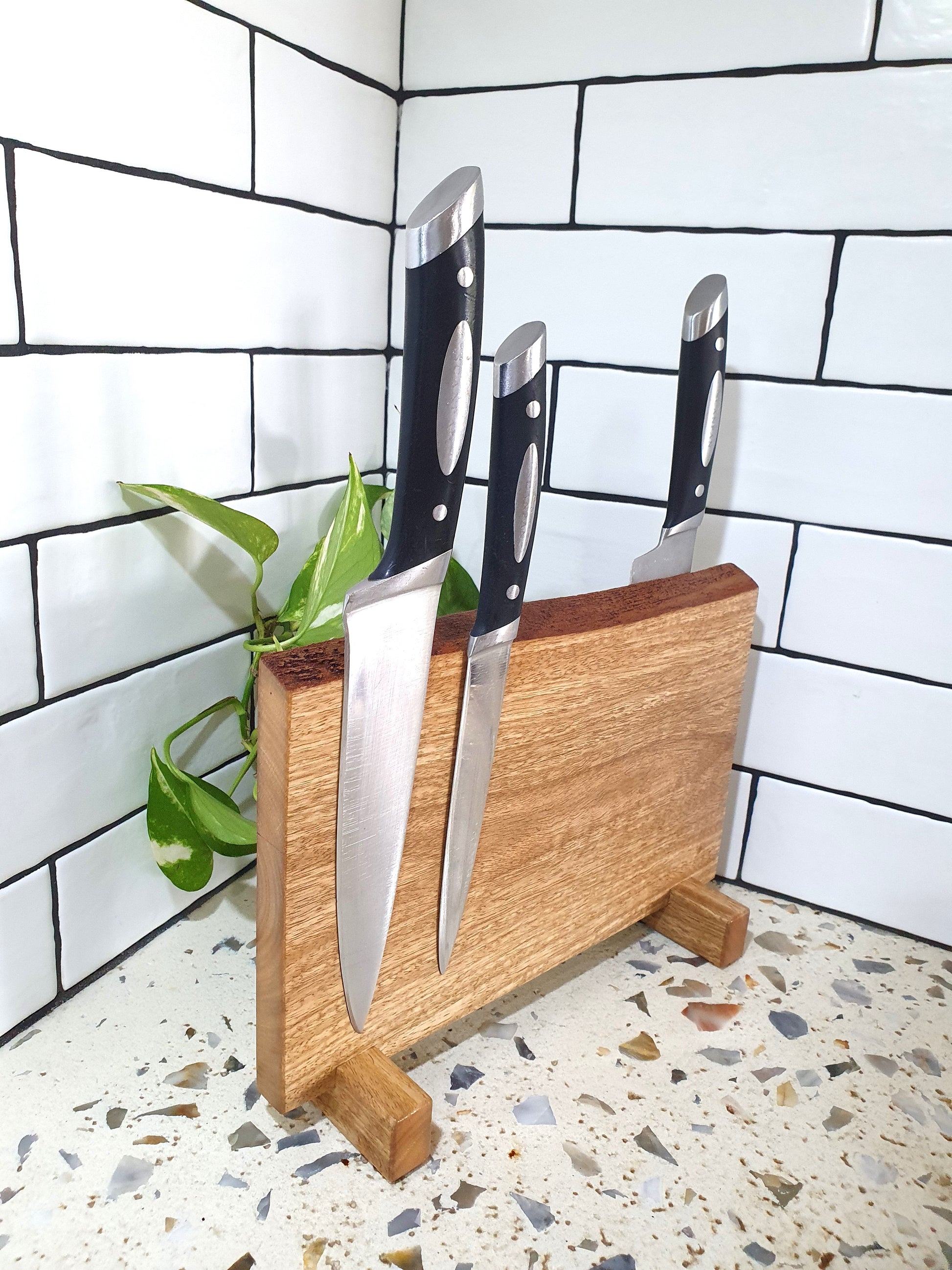 Wooden knife block with three knives on a tiled kitchen floor.