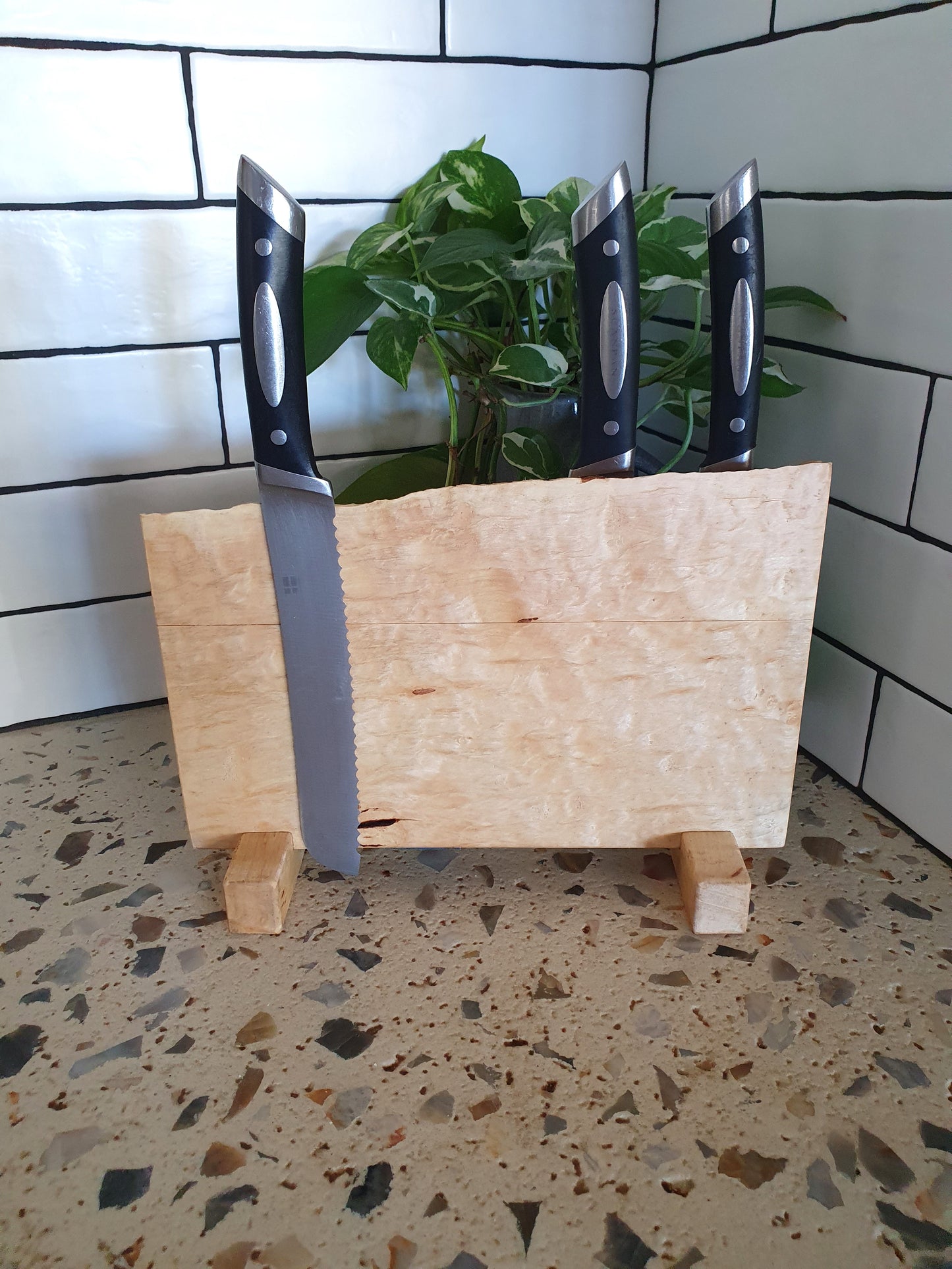 Wooden knife block with three knives on a speckled countertop.