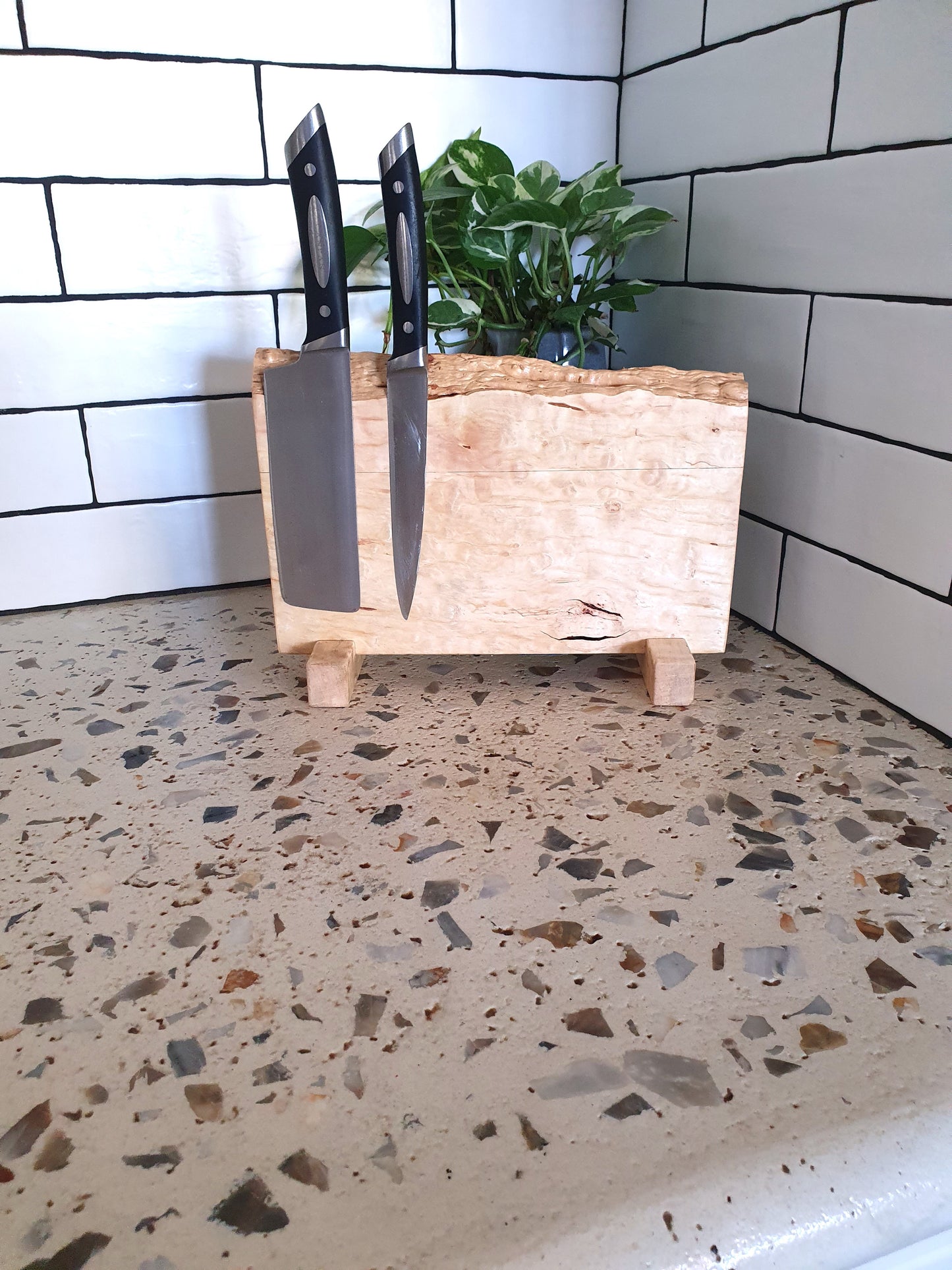 Wooden knife block with knives on a speckled countertop against a tiled wall.
