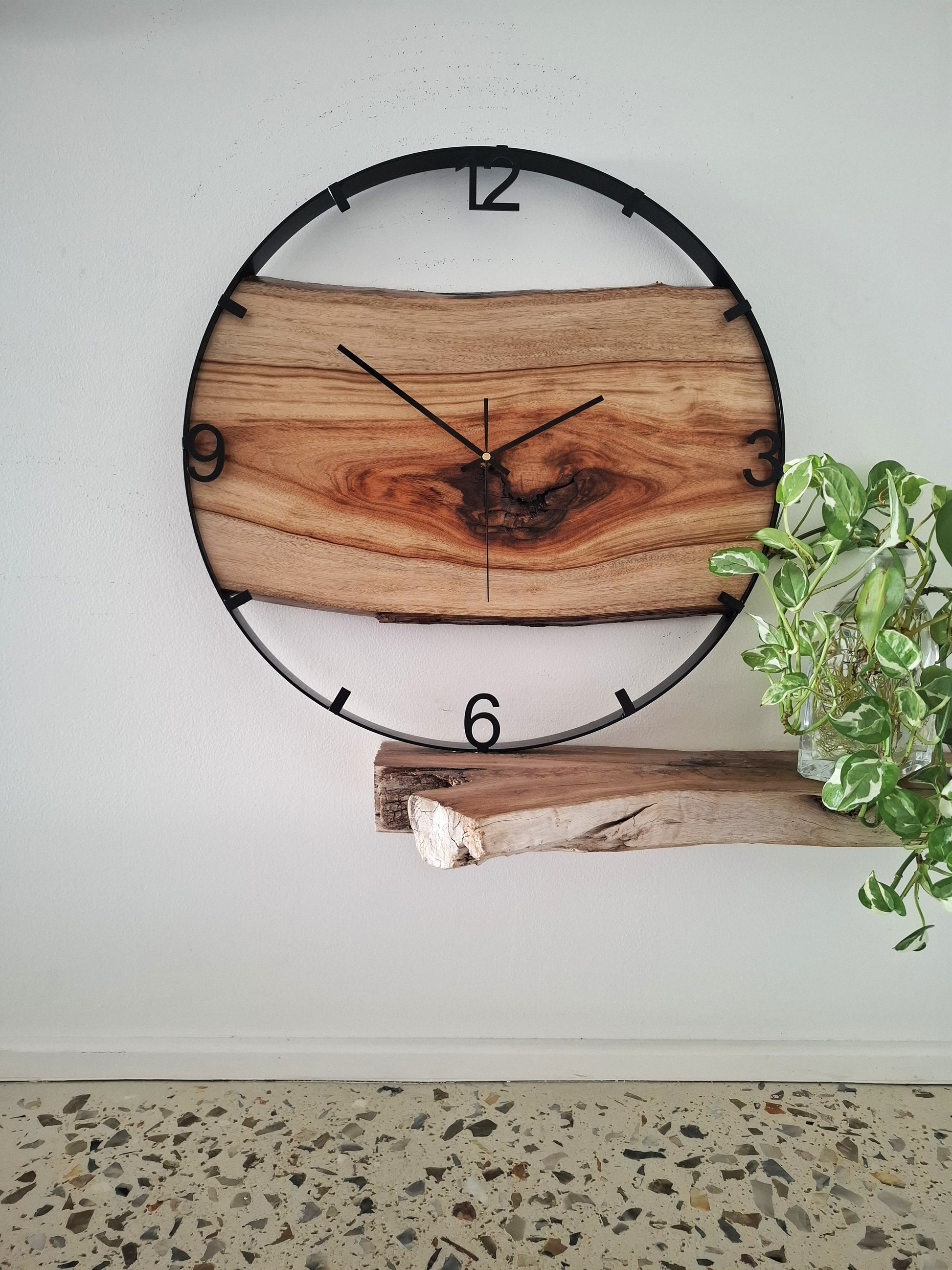 Wooden wall clock with natural finish and black metal frame on a white wall.