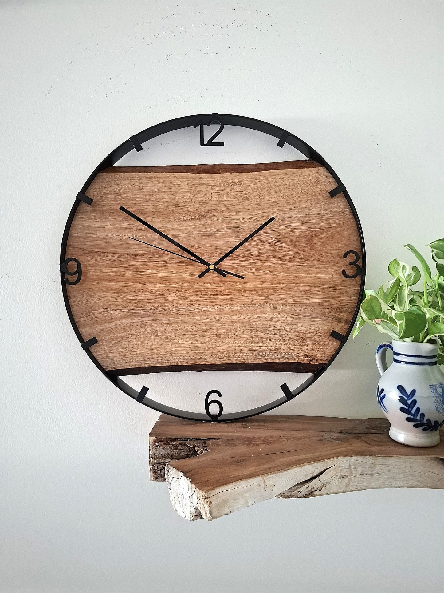 Wooden wall clock on a white background with a plant and decorative vase.