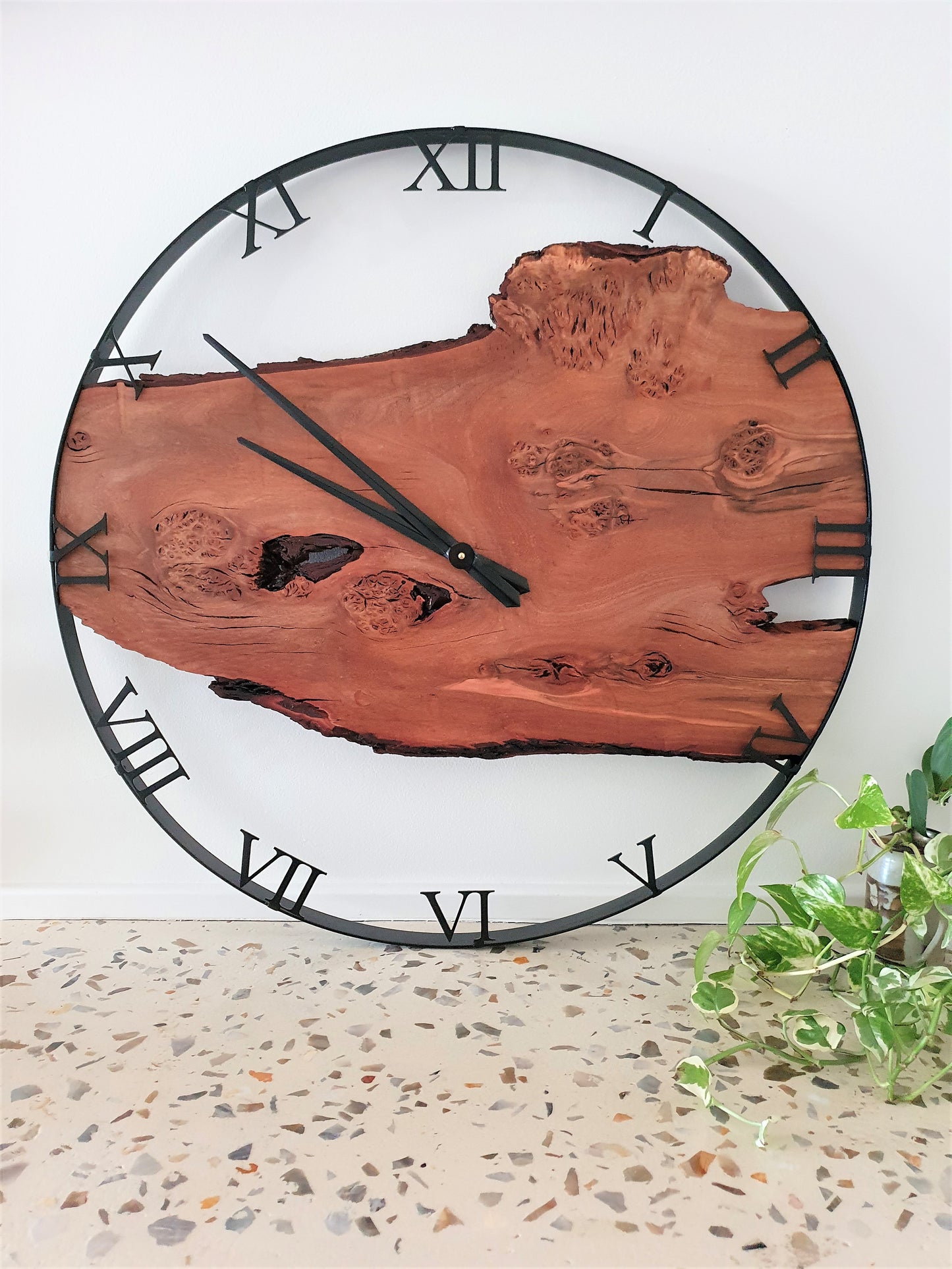 Wooden wall clock with natural finish and Roman numerals on a white wall.