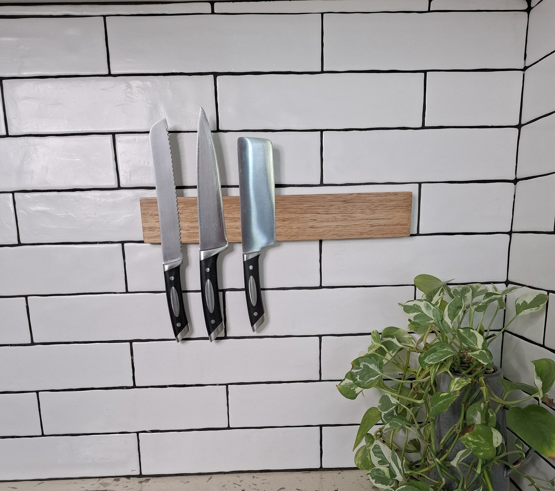 Wooden magnetic knife holder with knives on a tiled wall