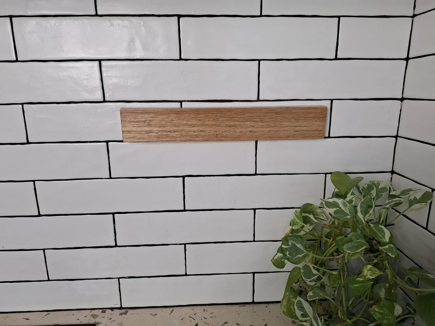 White tiled wall with a wooden shelf and a plant in the corner