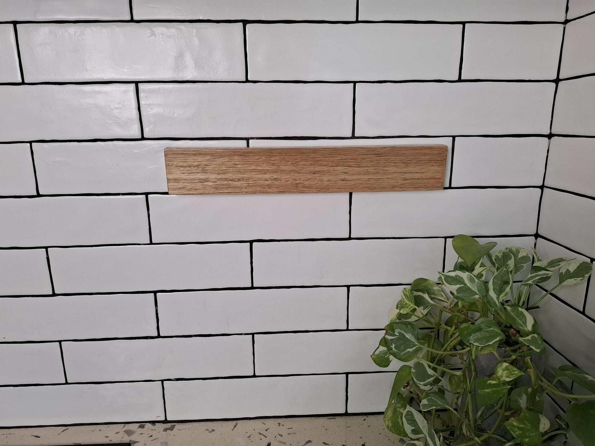 White tiled wall with a wooden shelf and a plant in the corner
