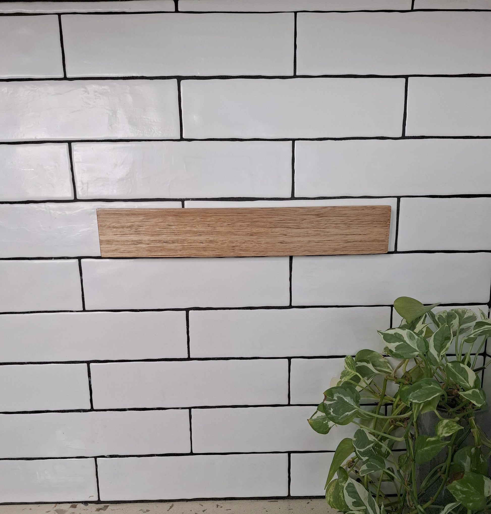 White tiled wall with a wooden strip and a plant in the corner