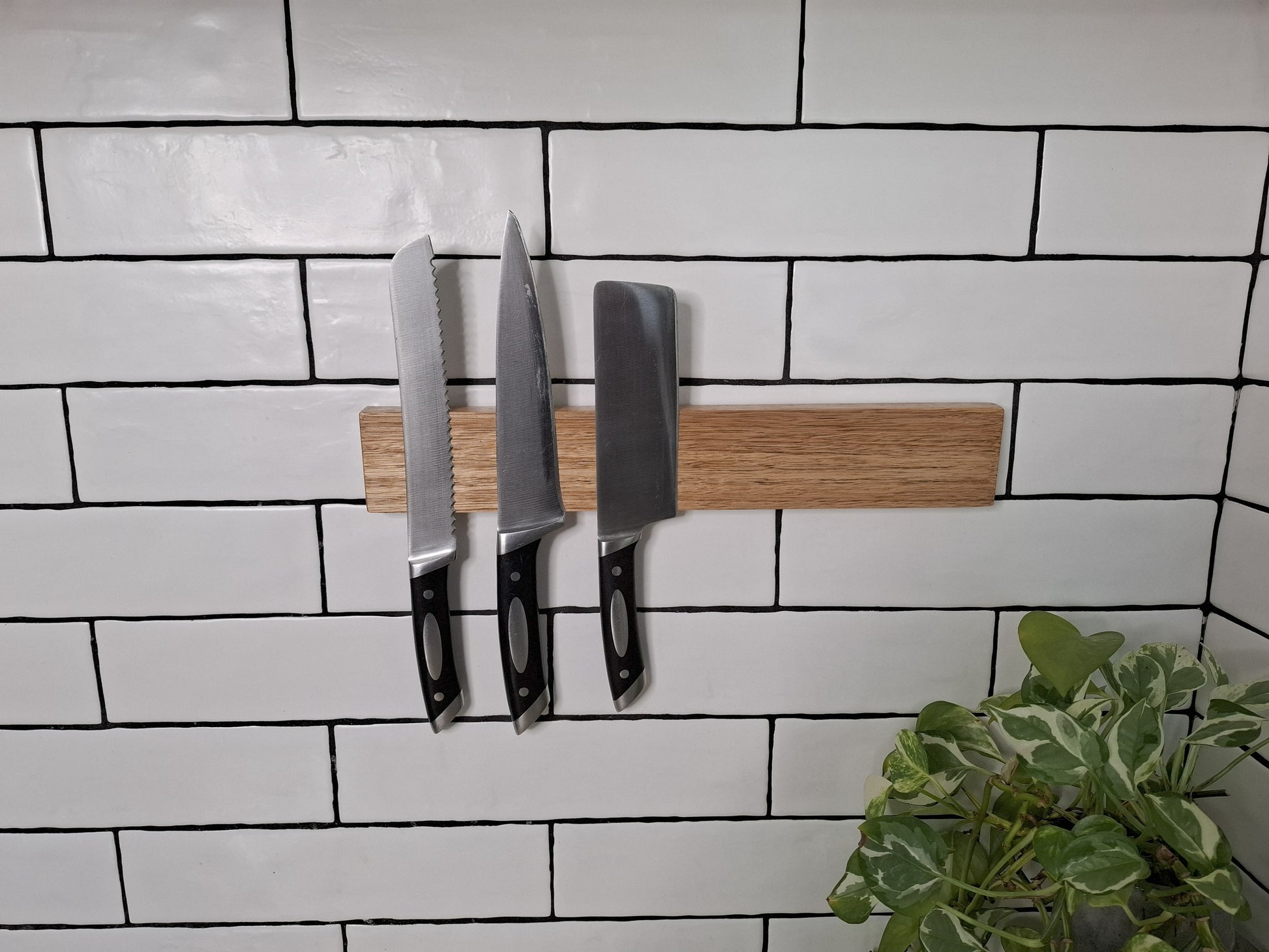 Set of knives on a magnetic knife holder against a tiled wall with a plant in the corner.