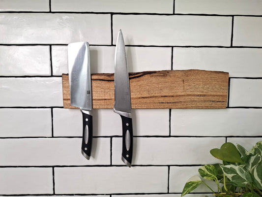 Three knives on a wooden magnetic strip against a white tiled wall.