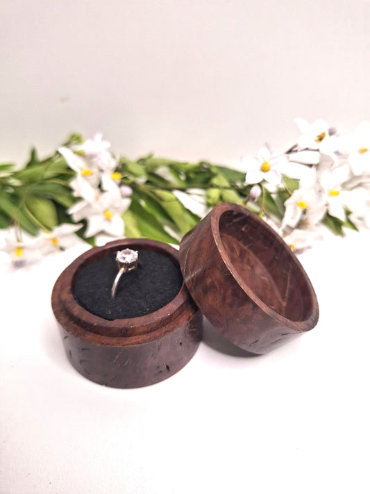Wooden ring box with a ring inside, surrounded by greenery and flowers on a white background