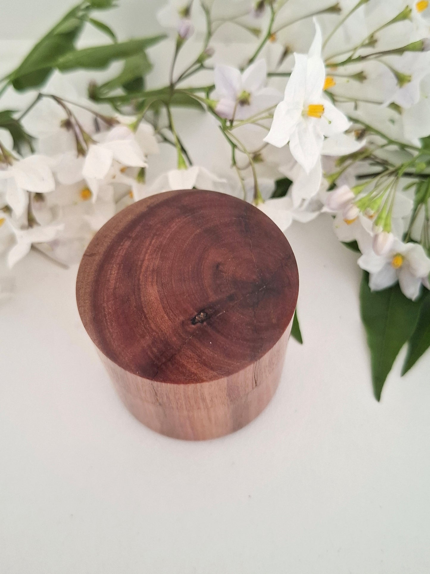 Wooden ring box with a lid on a white surface with flowers in the background