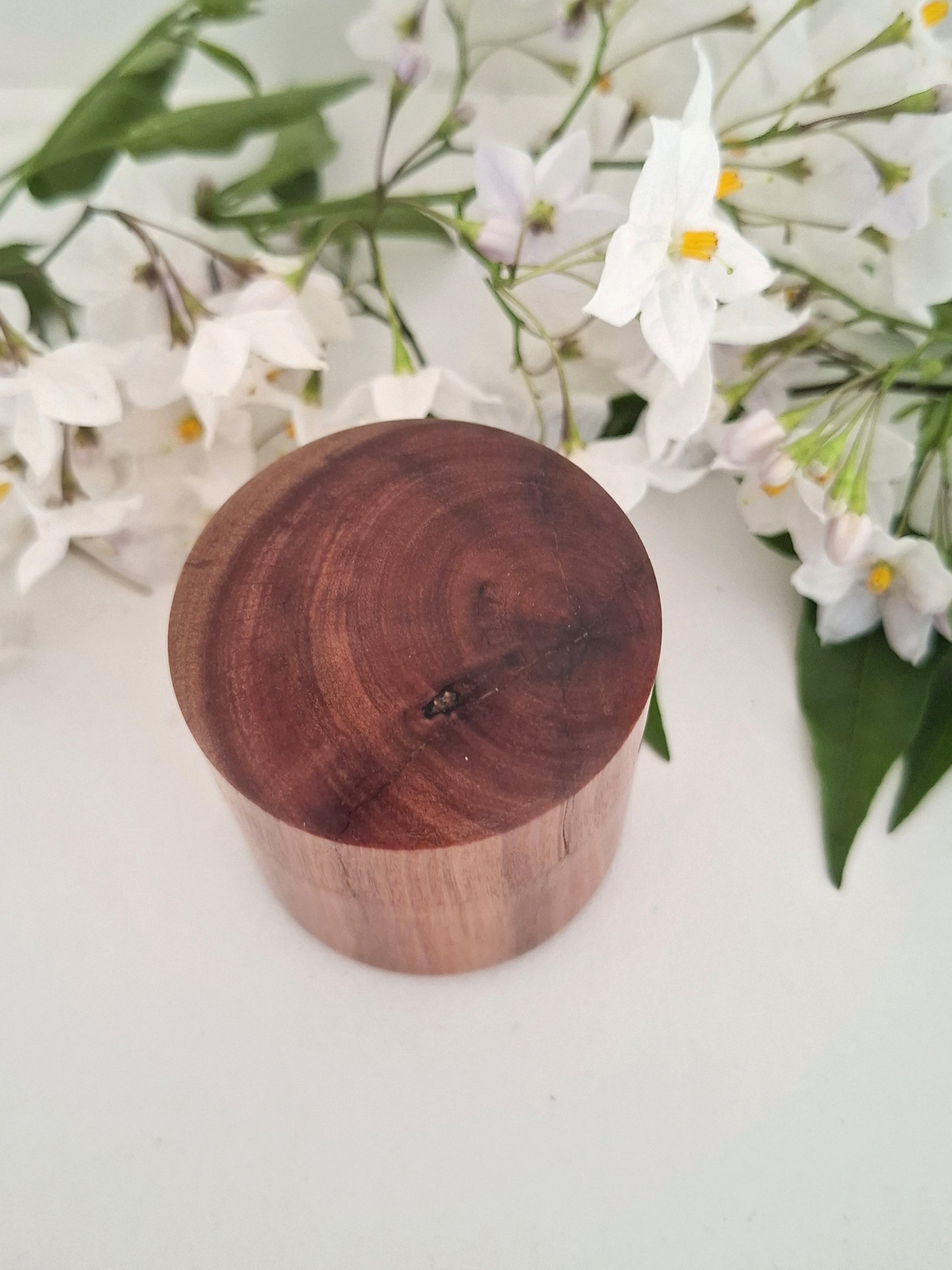 Wooden ring box with a lid on a white surface with flowers in the background