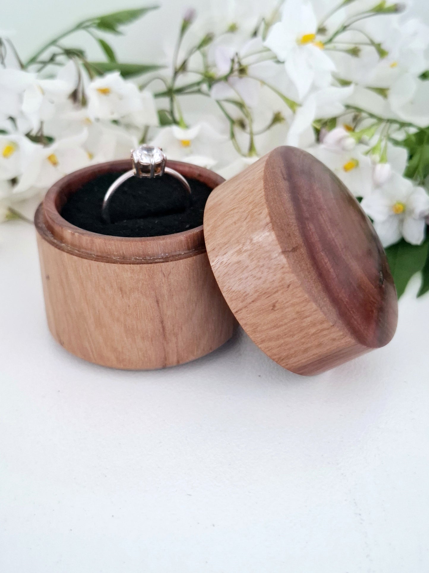 Wooden ring box with a ring inside, set against a white background with flowers.