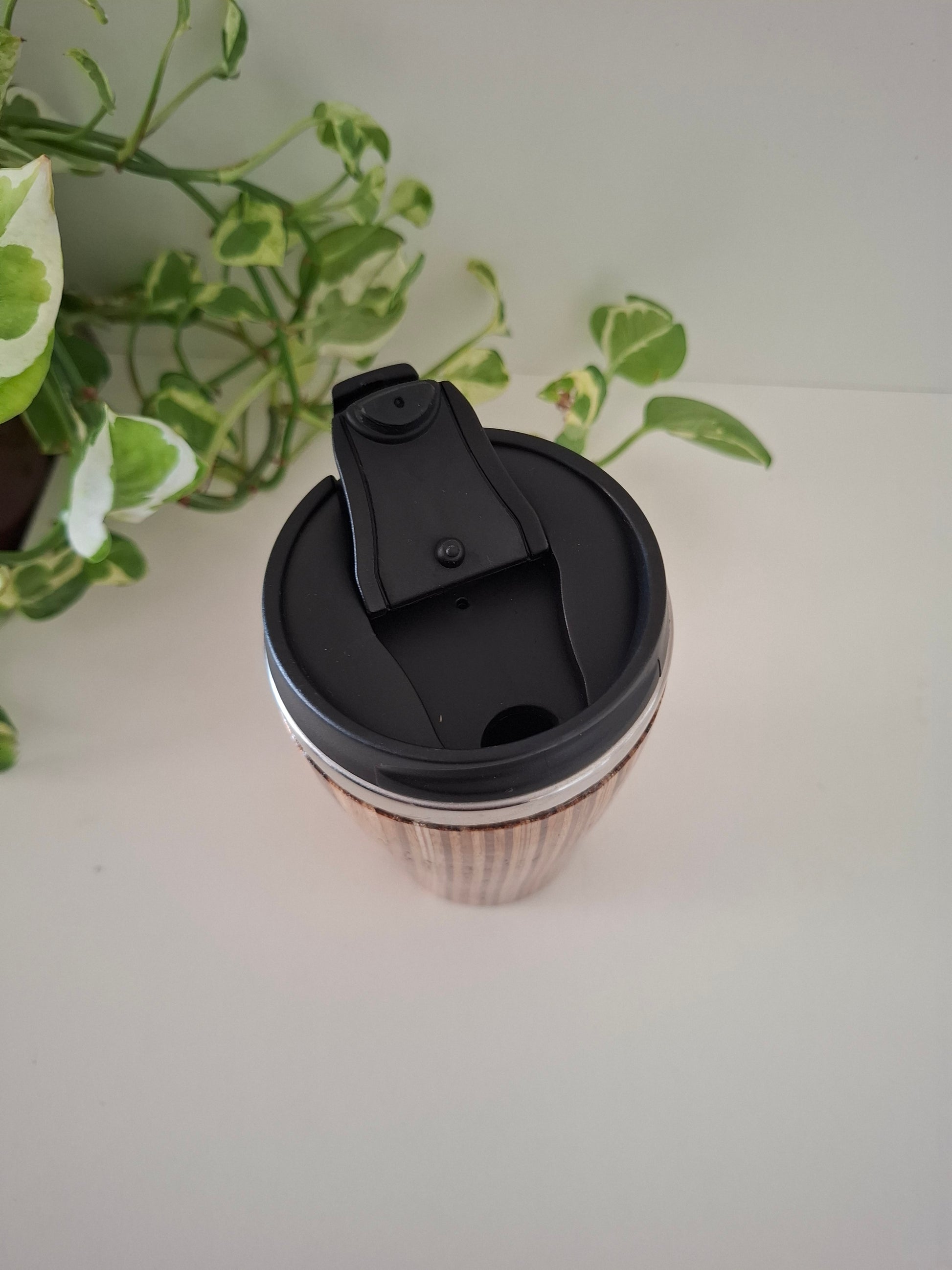 Black lid on a wooden cup against a light background with a plant in the corner