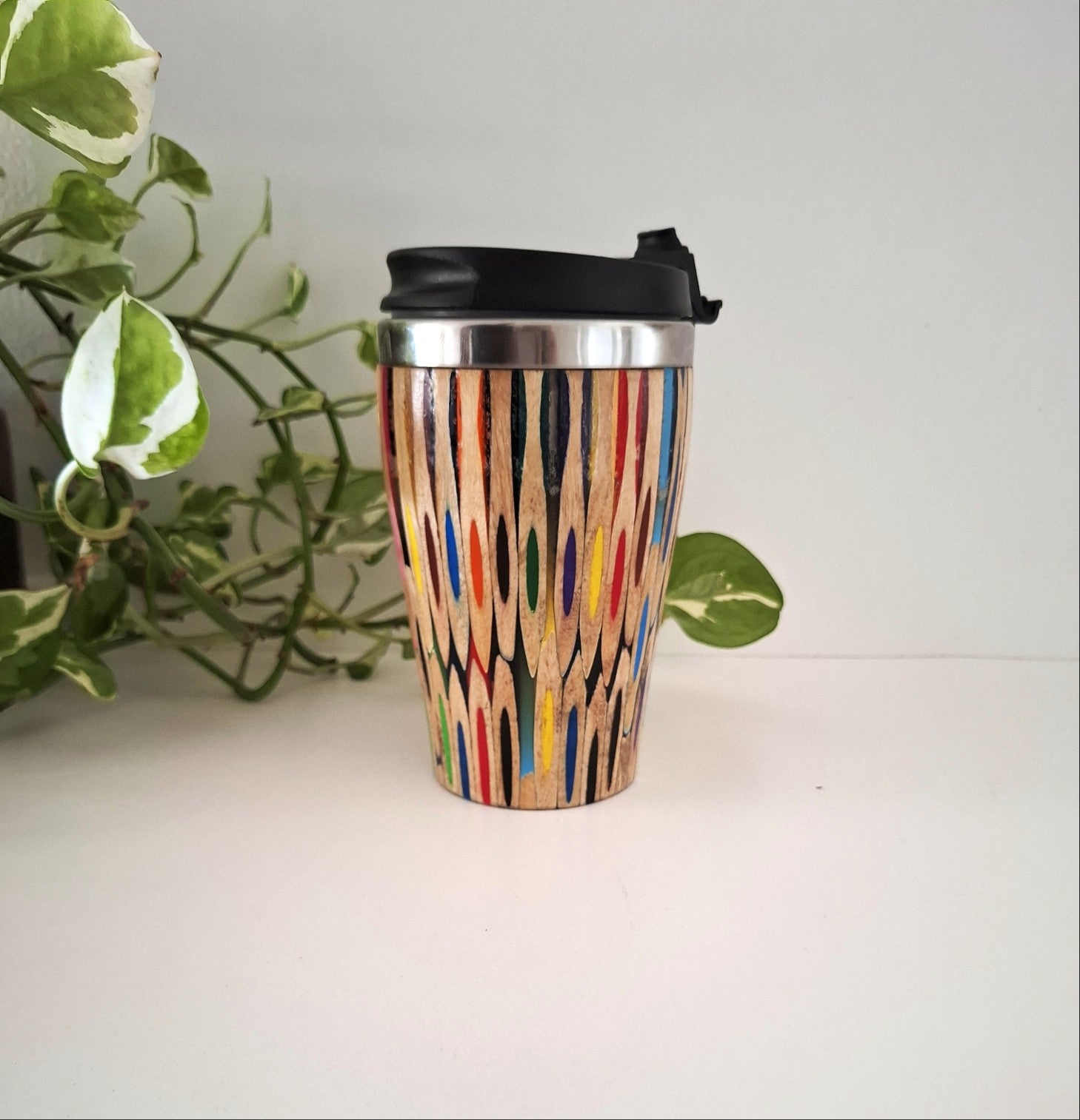 Coloured Pencil  travel mug on a white surface with a plant in the background