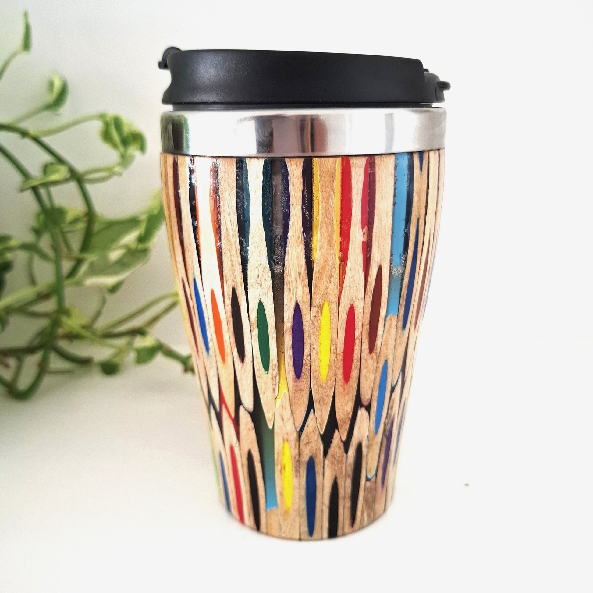 Coloured Pencil  travel mug on a white surface with a plant in the background