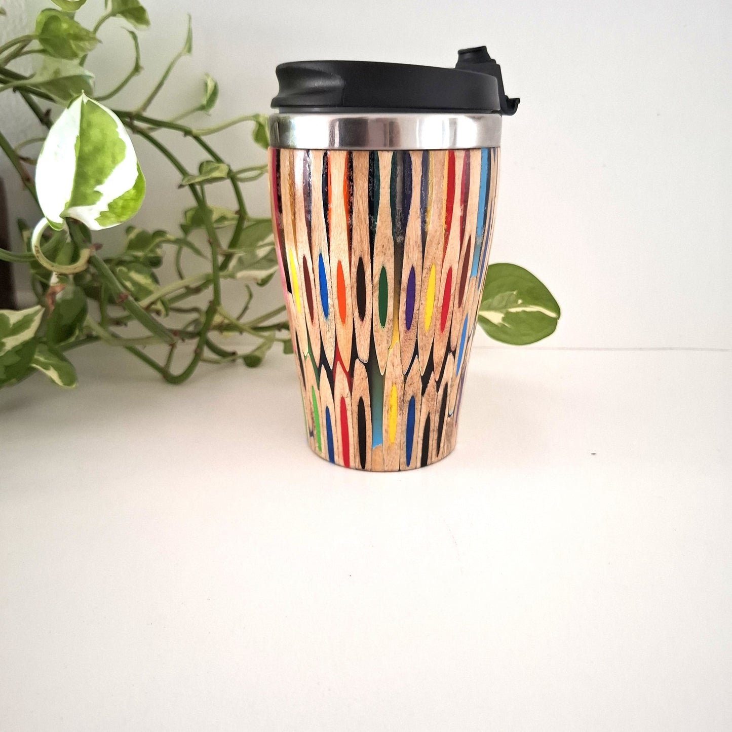 Coloured Pencil Reusable coffee cup with colorful pattern on a white surface with a plant in the background