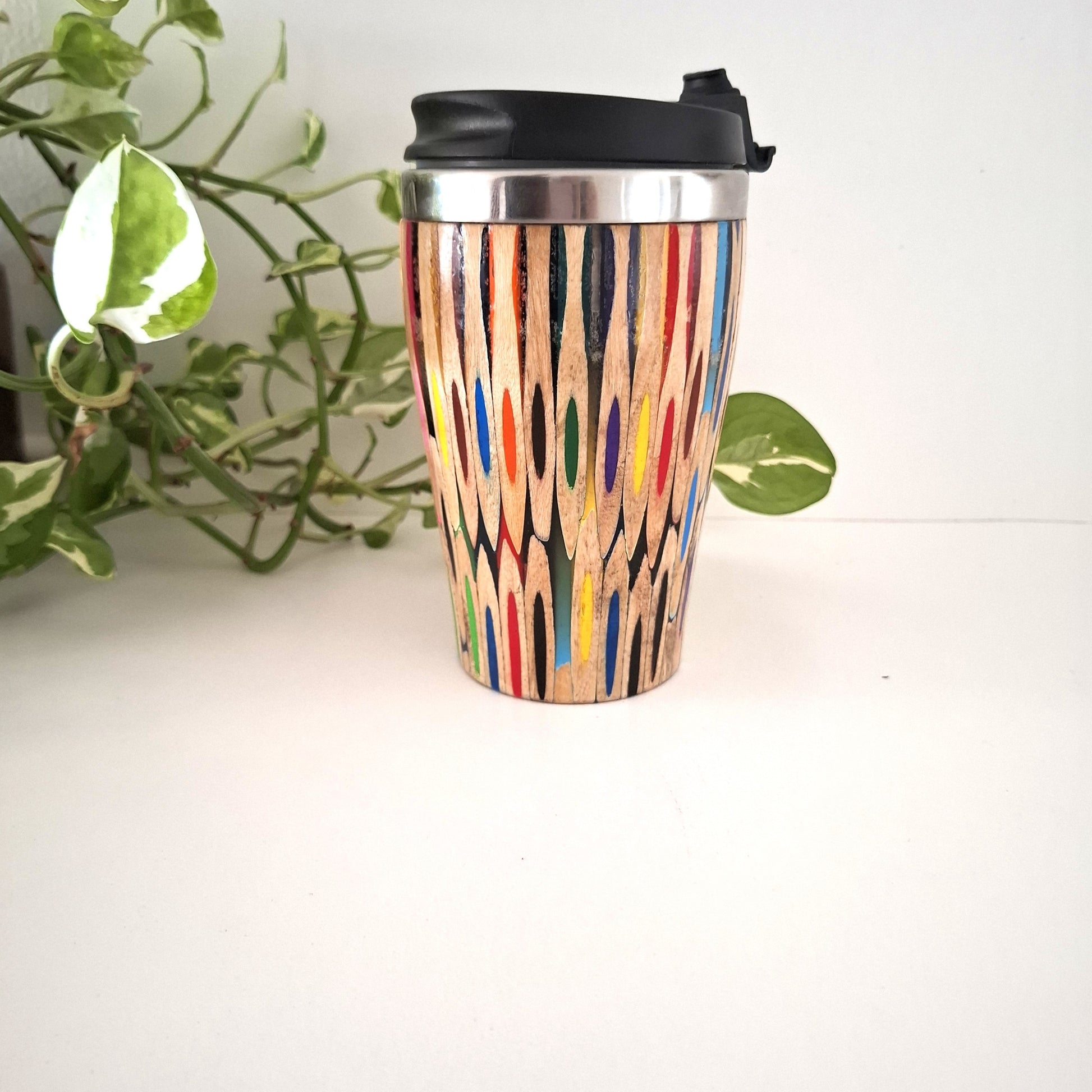 Coloured Pencil Reusable coffee cup with colorful pattern on a white surface with a plant in the background