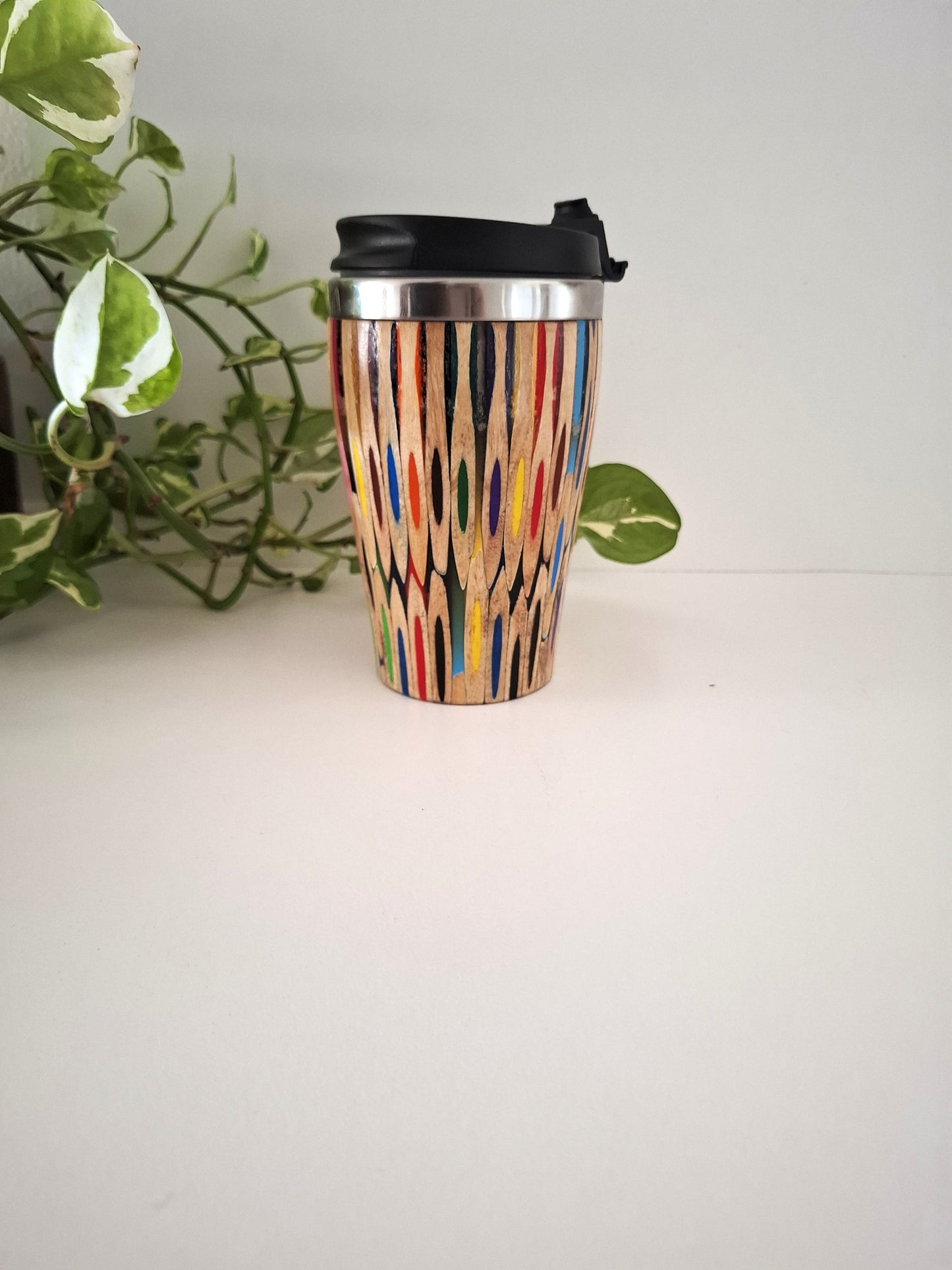 Coloured Pencil  travel mug on a white surface with a plant in the background