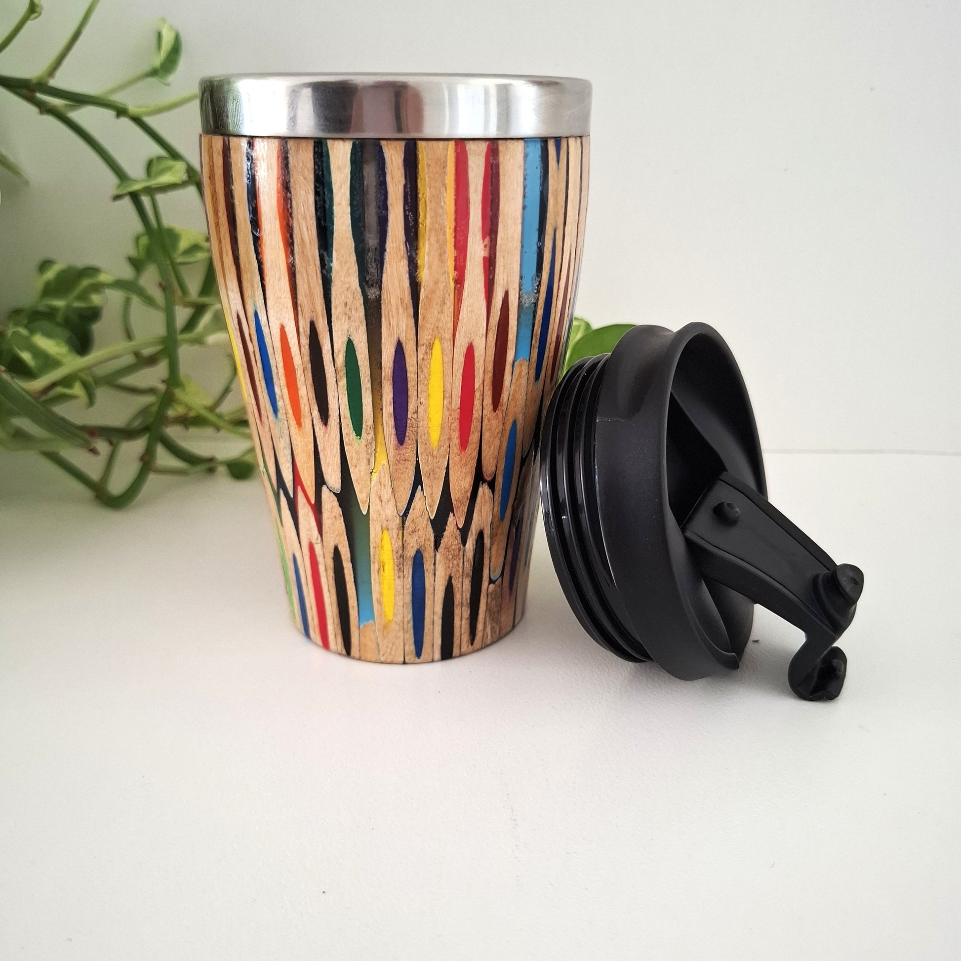 Wooden tumbler with colorful patterns and a black lid on a white surface.