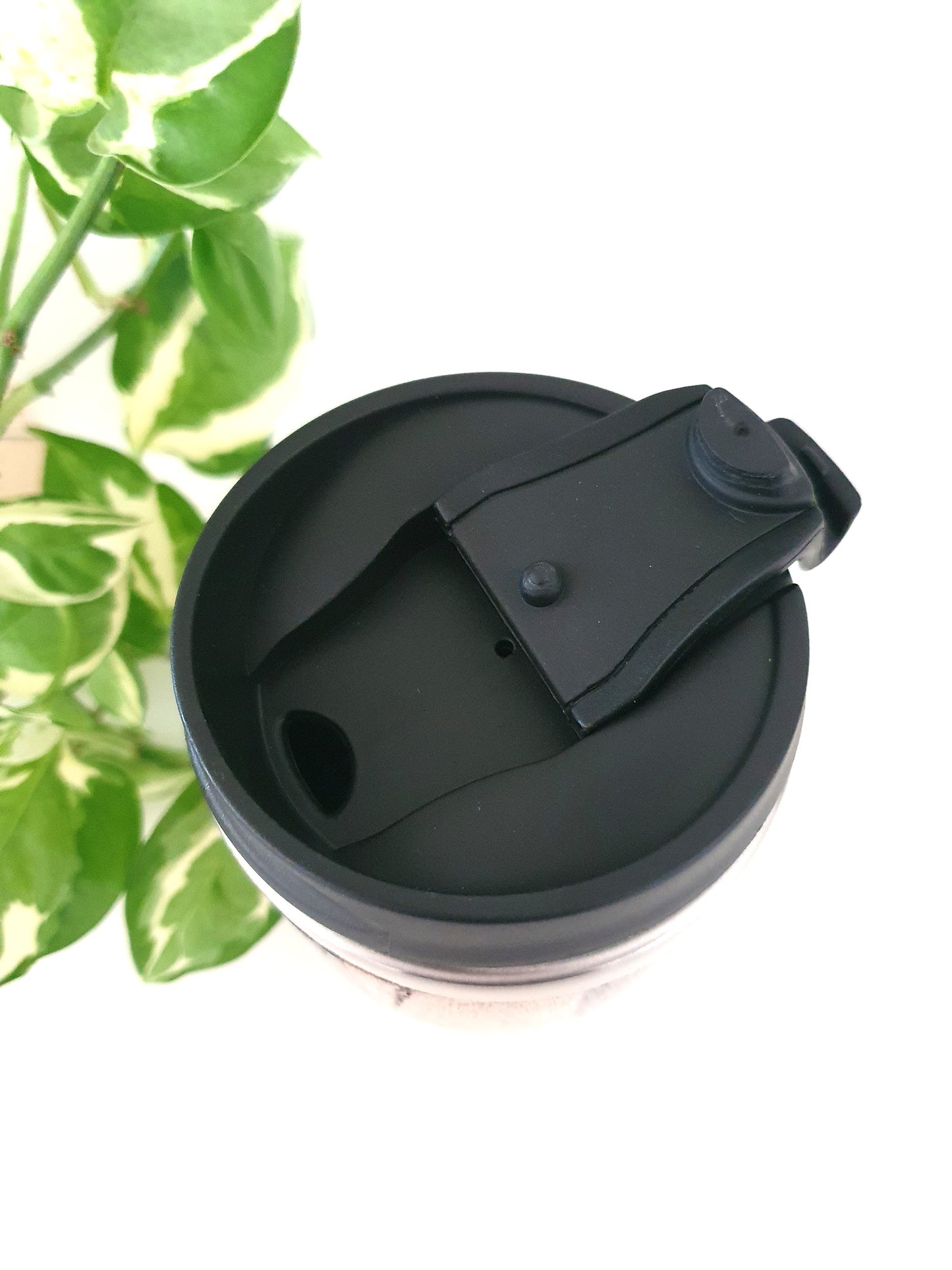 Black lid on a clear cup with green leaves in the background