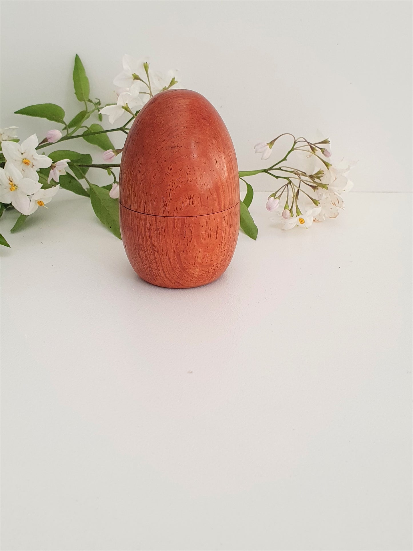 Wooden egg-shaped container with a textured surface on a light background with white flowers and green leaves.