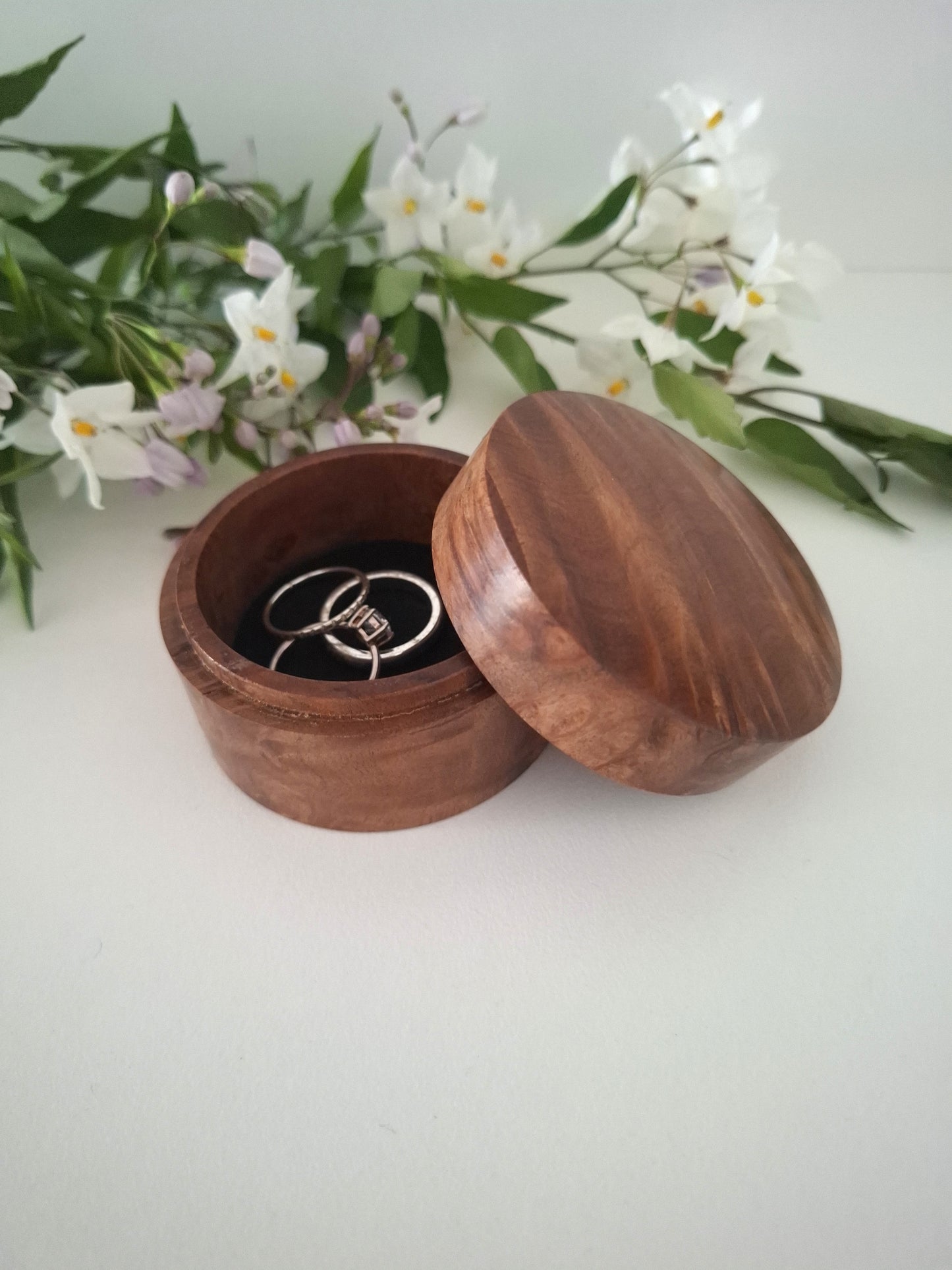Wooden ring box with a ring inside, placed on a white surface with greenery in the background.