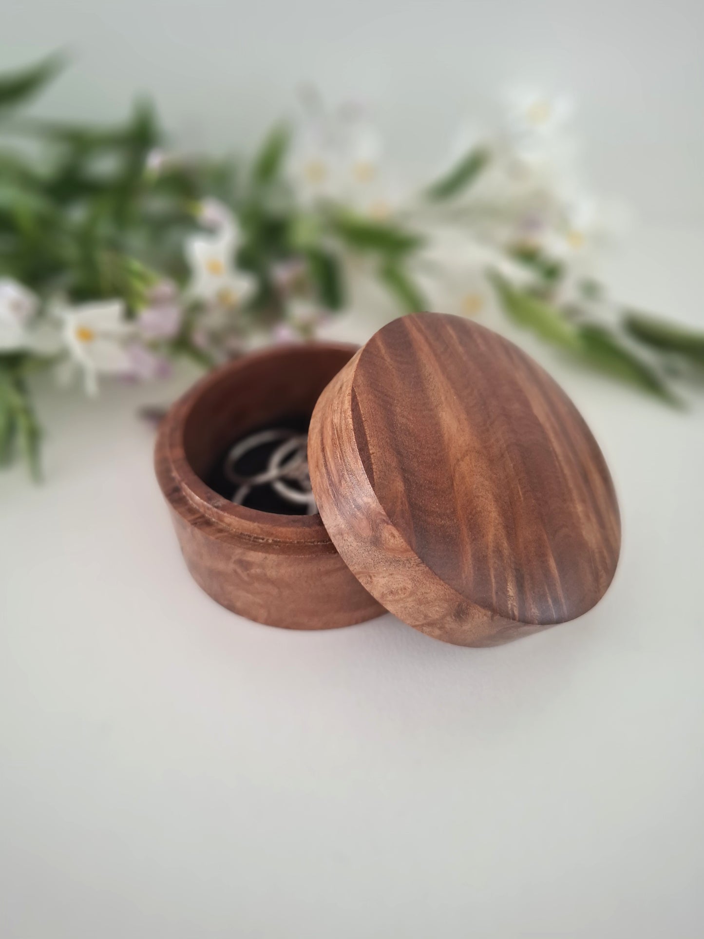 Wooden ring box with a lid on a light background with greenery