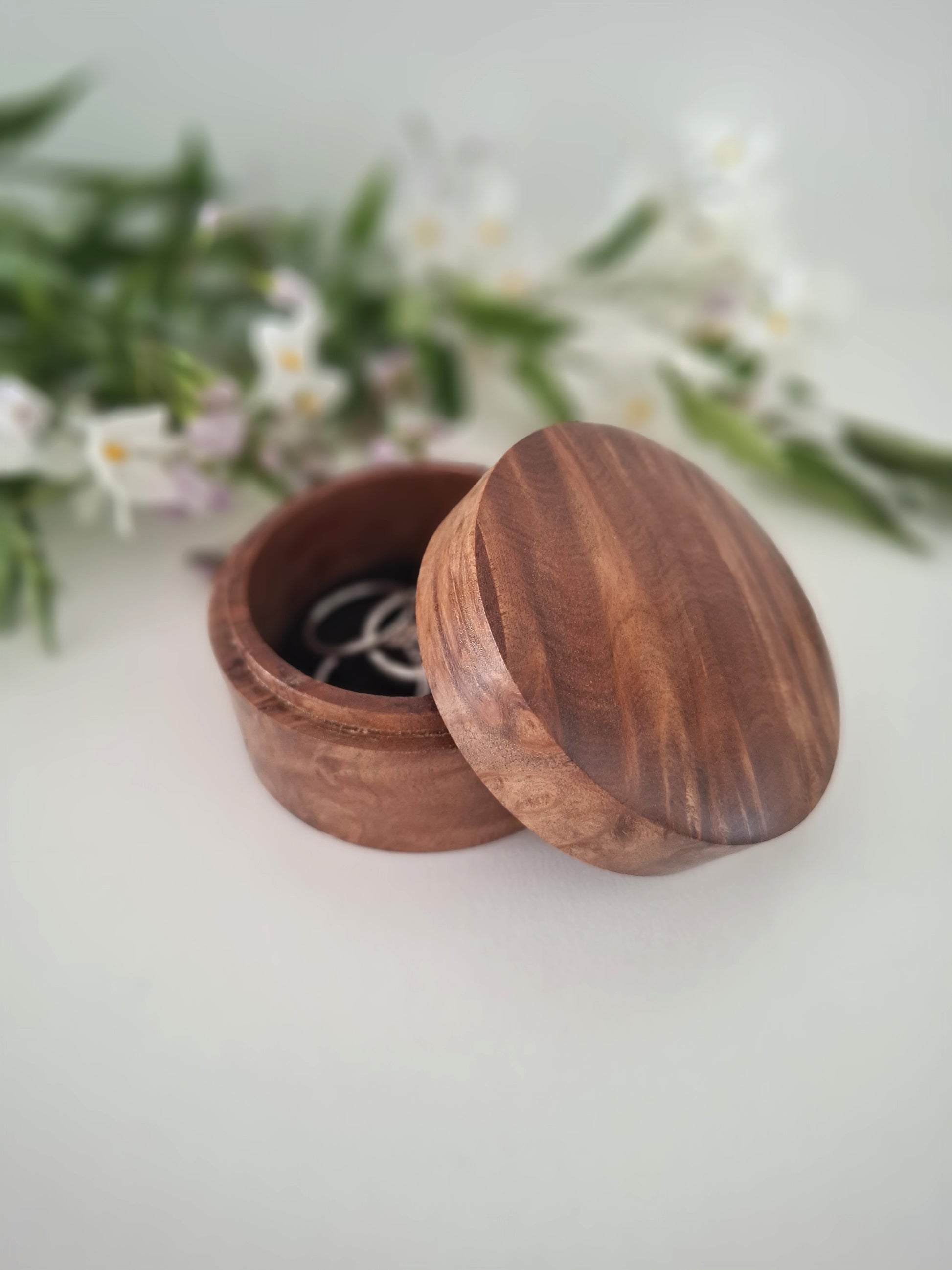 Wooden ring box with a lid on a light background with greenery