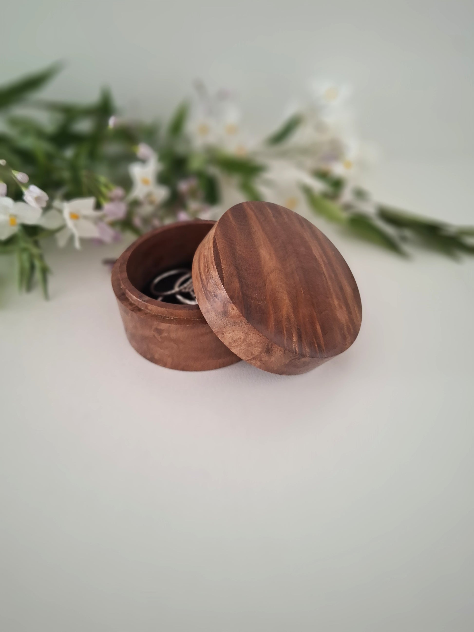 Wooden jewelry box with a lid open on a light background with greenery.