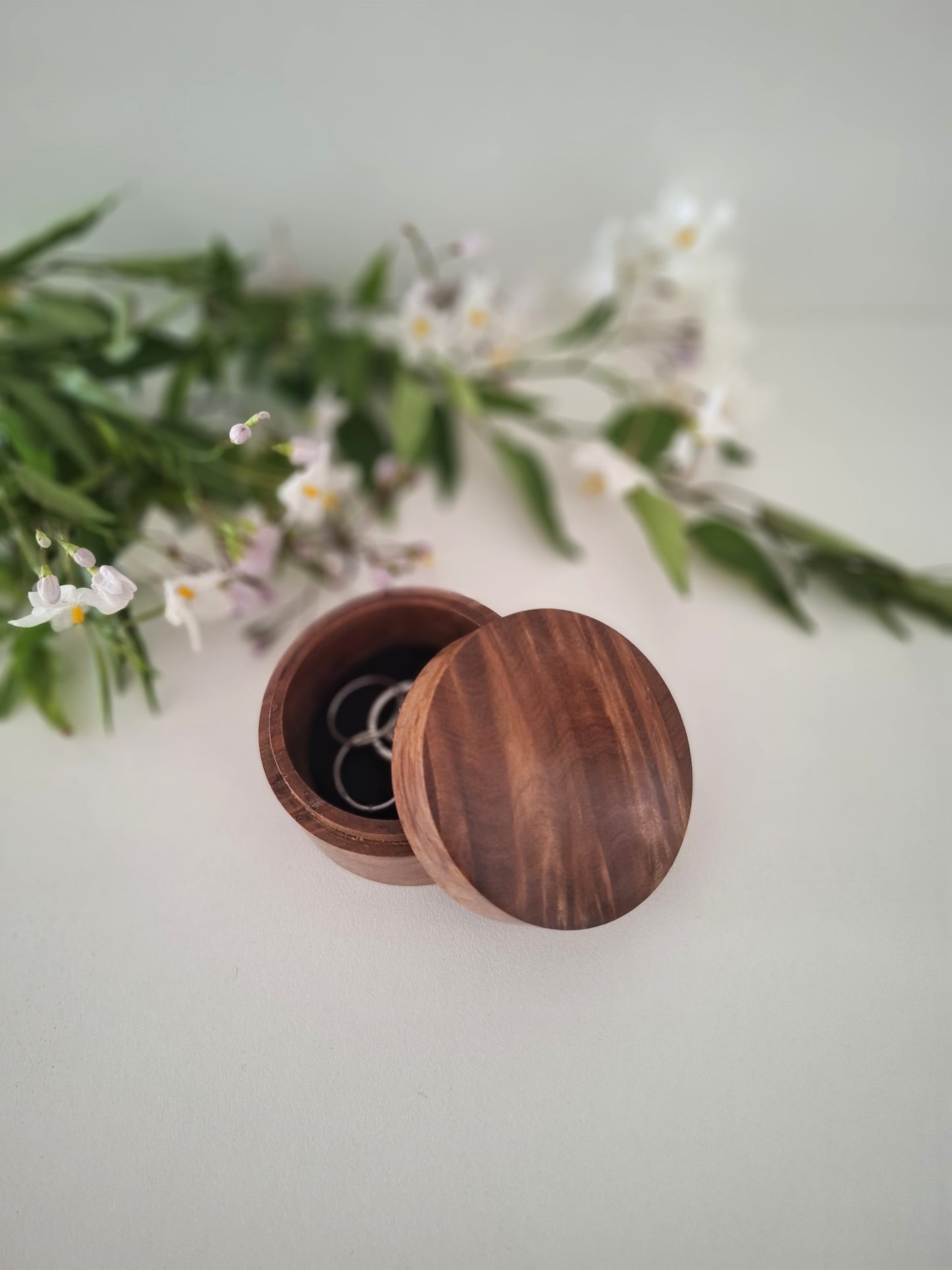 Wooden jewelry box with a lid open, revealing an earring, on a light background with greenery.