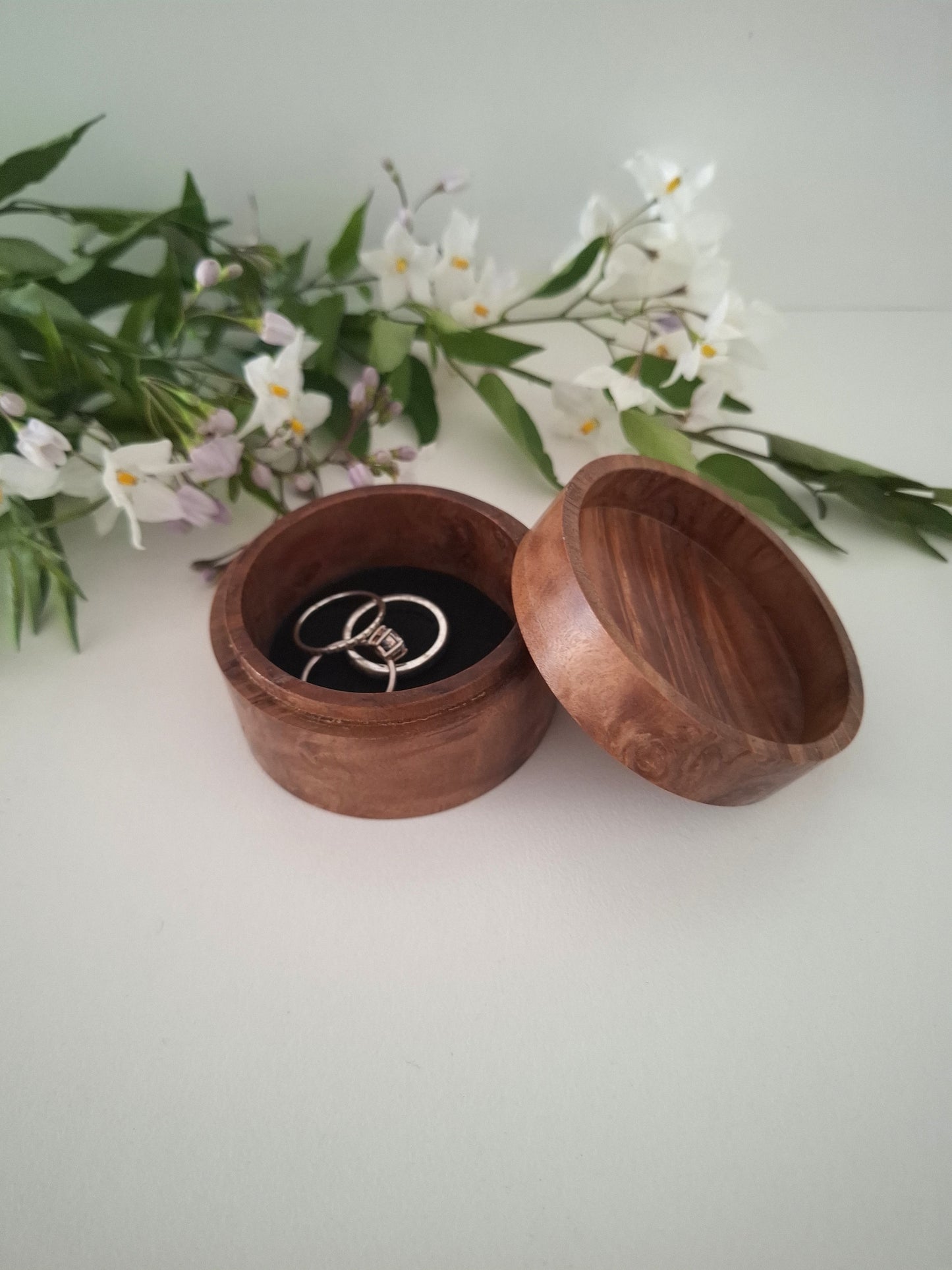 Wooden ring box with a ring inside, surrounded by flowers on a light background