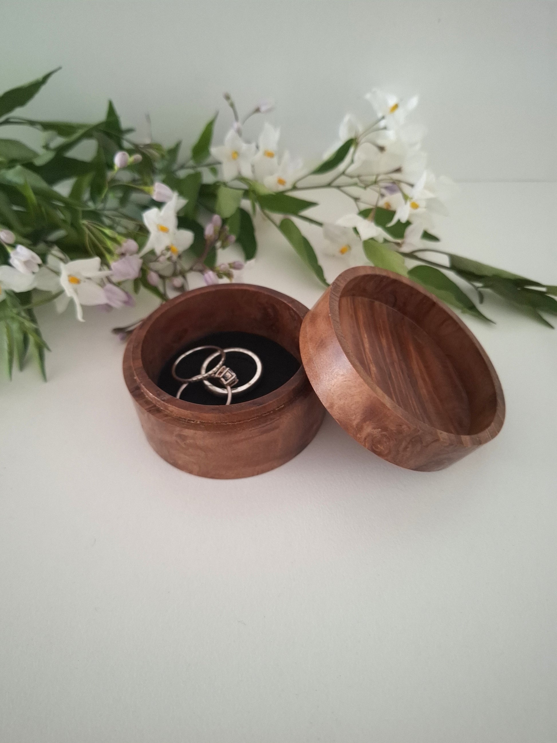 Wooden ring box with a ring inside, surrounded by flowers on a light background