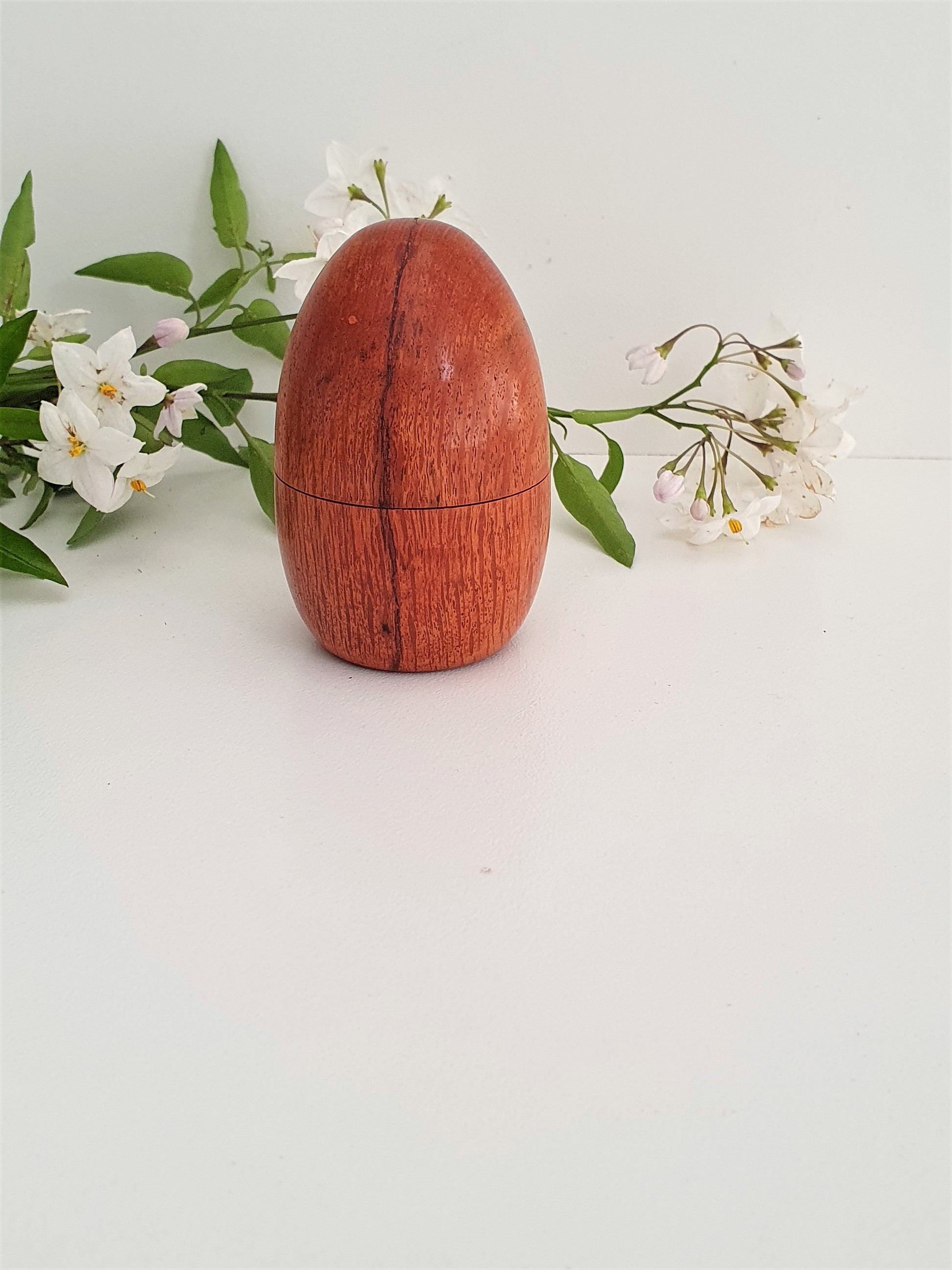 Wooden egg-shaped container with a lid on a light background with flowers.