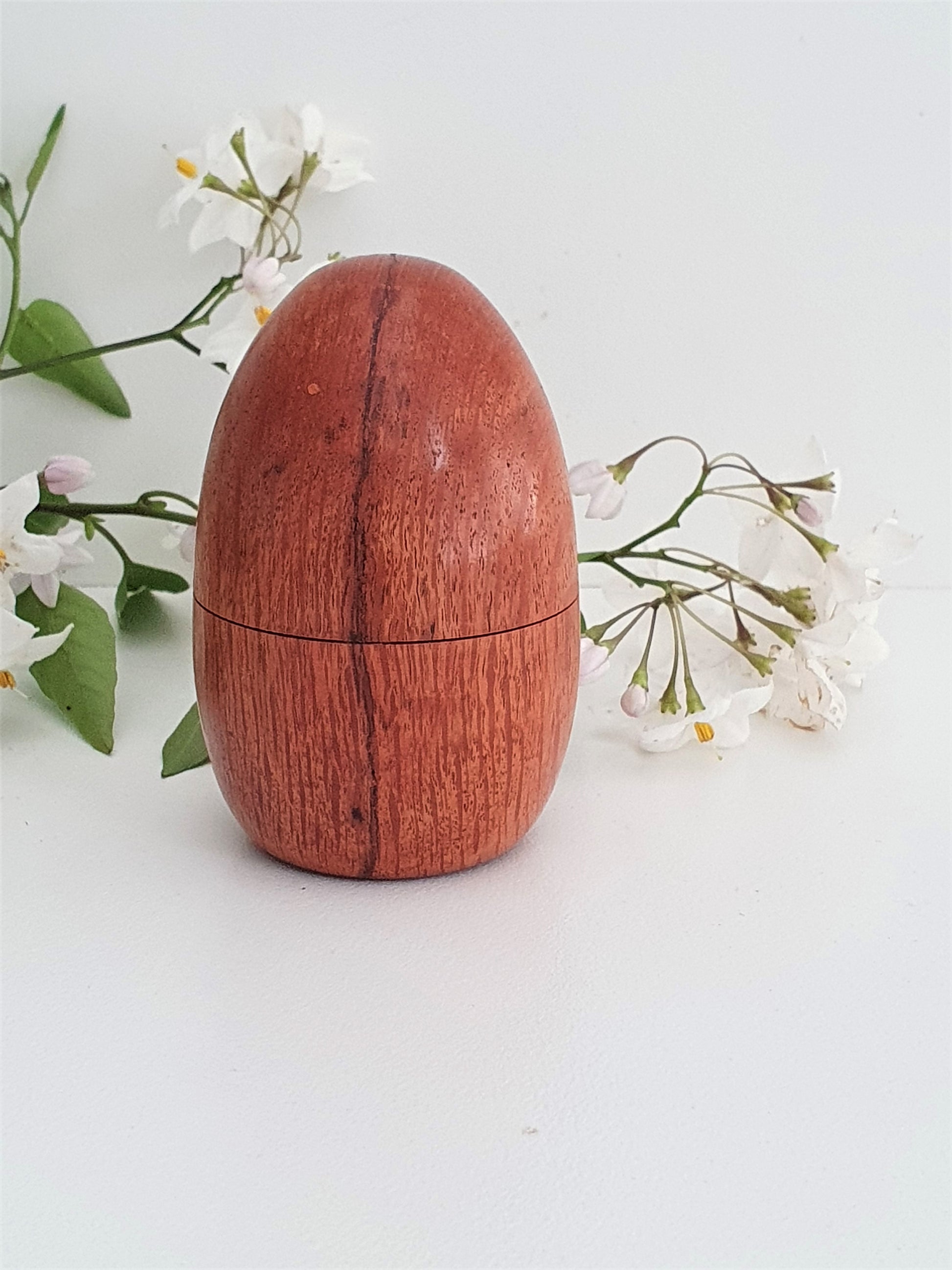 Wooden egg-shaped container with a lid on a light background with flowers.
