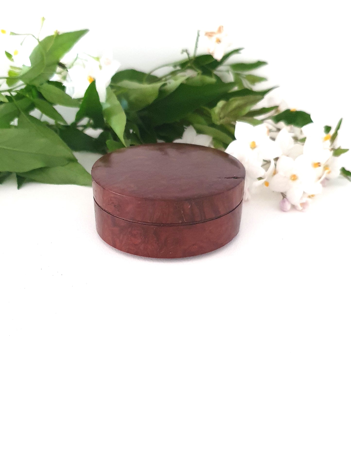 Round wooden box with a textured surface on a white background with green leaves and flowers.